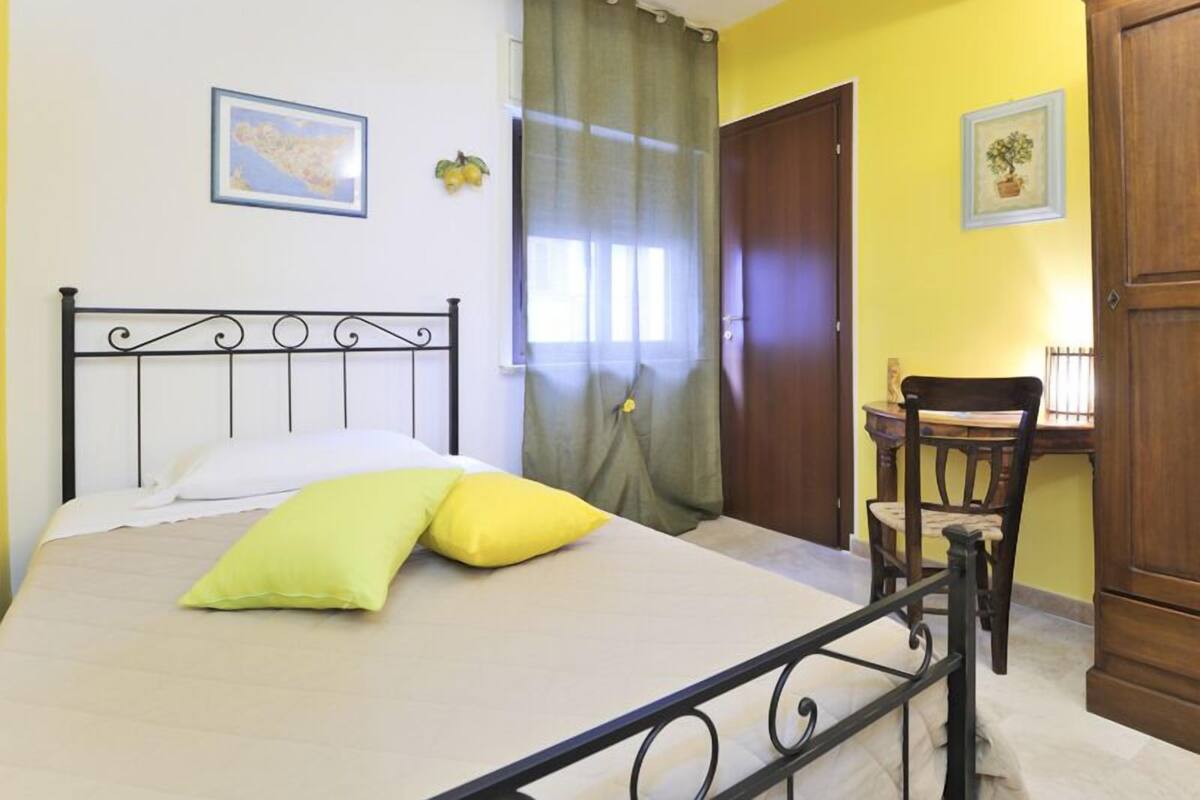 Un dormitorio con cama, una silla, un armario y una ventana con cortinas.