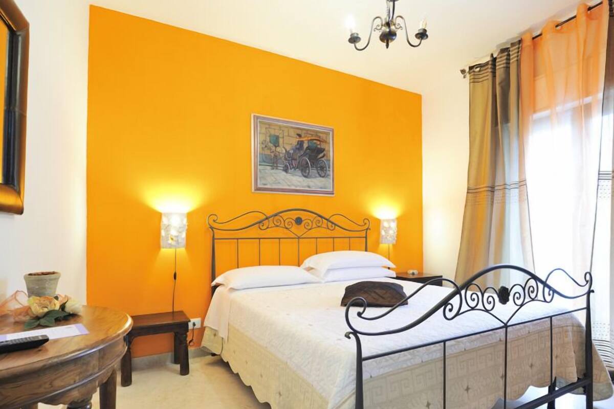 Un dormitorio con una cama, dos lámparas de noche, un cuadro en la pared y una ventana con cortinas.
