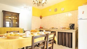 A dining area with a yellow tablecloth, wooden chairs, and a kitchen counter with appliances. - La Casa Di Evita (Carini)