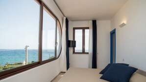Quarto com uma janela grande, cama com almofadas azuis, televisão de tela plana e porta com moldura azul.