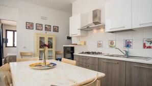 Cozinha moderna com armários brancos, fogão a gás e uma pia. Há uma mesa de jantar com cadeiras e um vaso com flores.