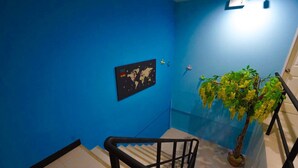 A blue-walled stairwell with a black railing, a world map, and a potted plant with yellow flowers. - Plu Garden Villa (Bangkok)