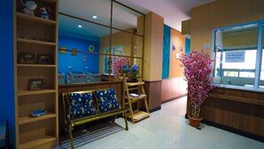 A reception area with a wooden bench, shelves with various items, a potted plant, and a window with a view. - Plu Garden Villa (Bangkok)