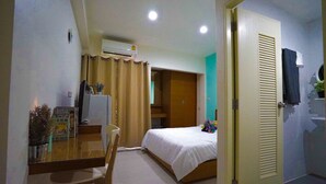 A hotel room with a bed, a desk with a chair, an air conditioning unit, a door, and a bathroom with a towel hanging on the wall. - Plu Garden Villa (Bangkok)