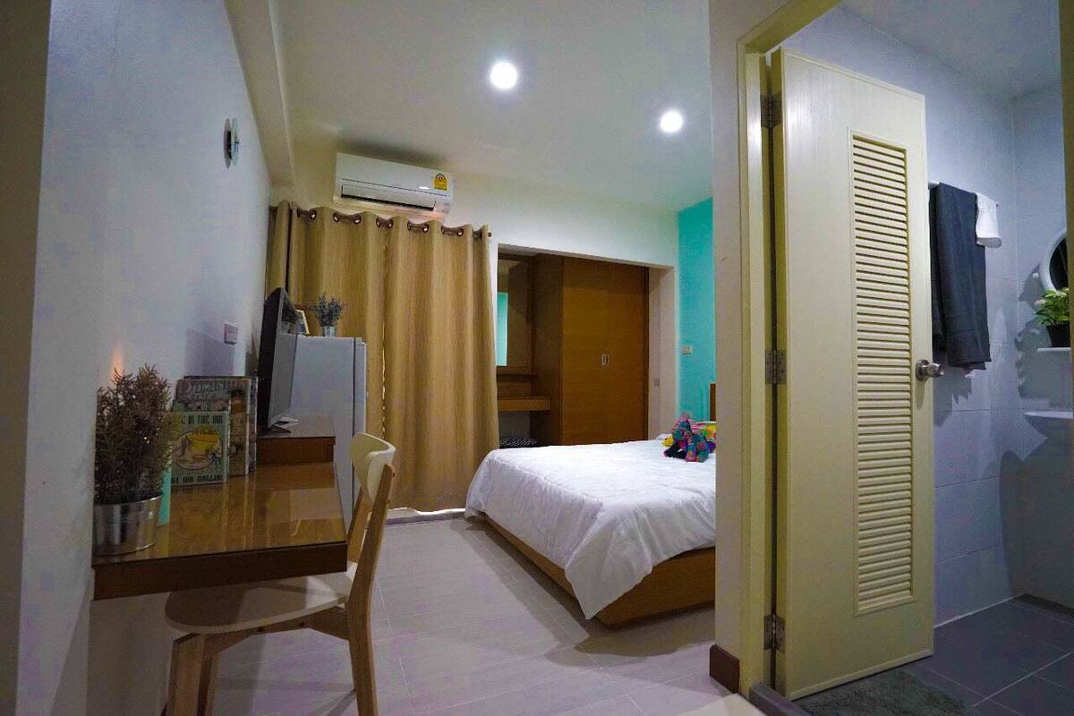 Ein Hotelzimmer mit Bett, Schreibtisch mit Stuhl, Klimaanlage, einer Tür und einem Badezimmer mit Handtuch an der Wand.
