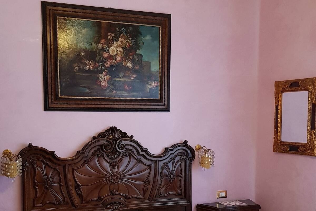 A bedroom with a large bed, a chandelier, a framed painting, and a mirror.