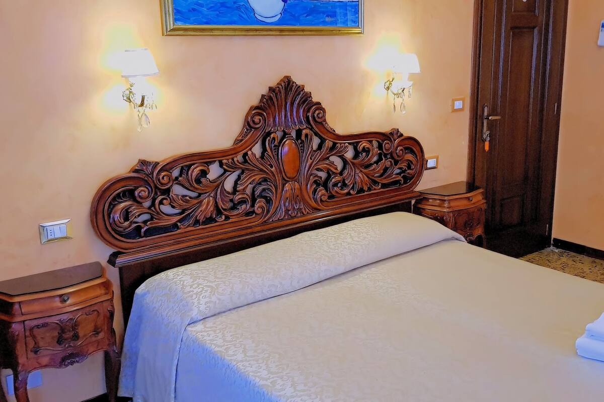 A neatly made bed with a decorative headboard, two bedside tables, and wall-mounted lamps.