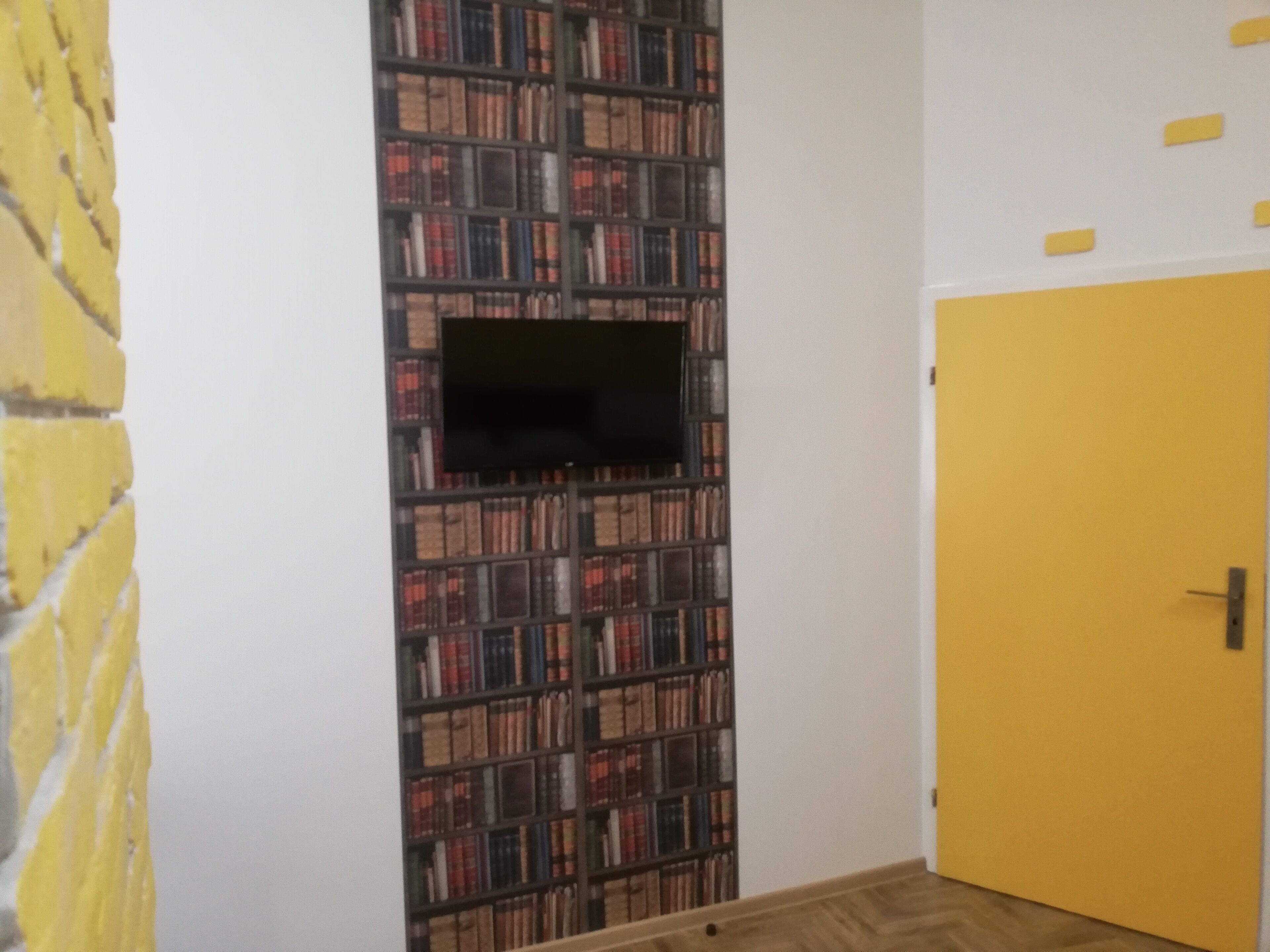 A room with a bookshelf, a television mounted on the wall, and a yellow door.