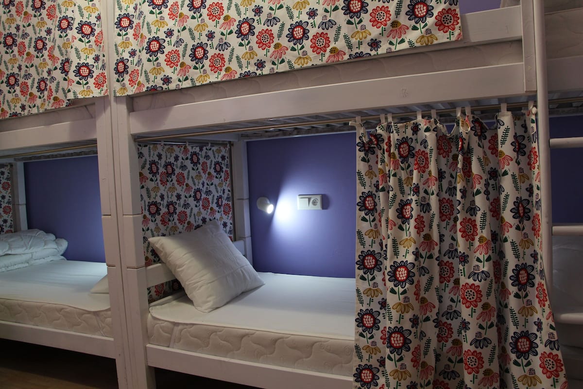 A bunk bed room with floral-patterned curtains and a wall-mounted light.