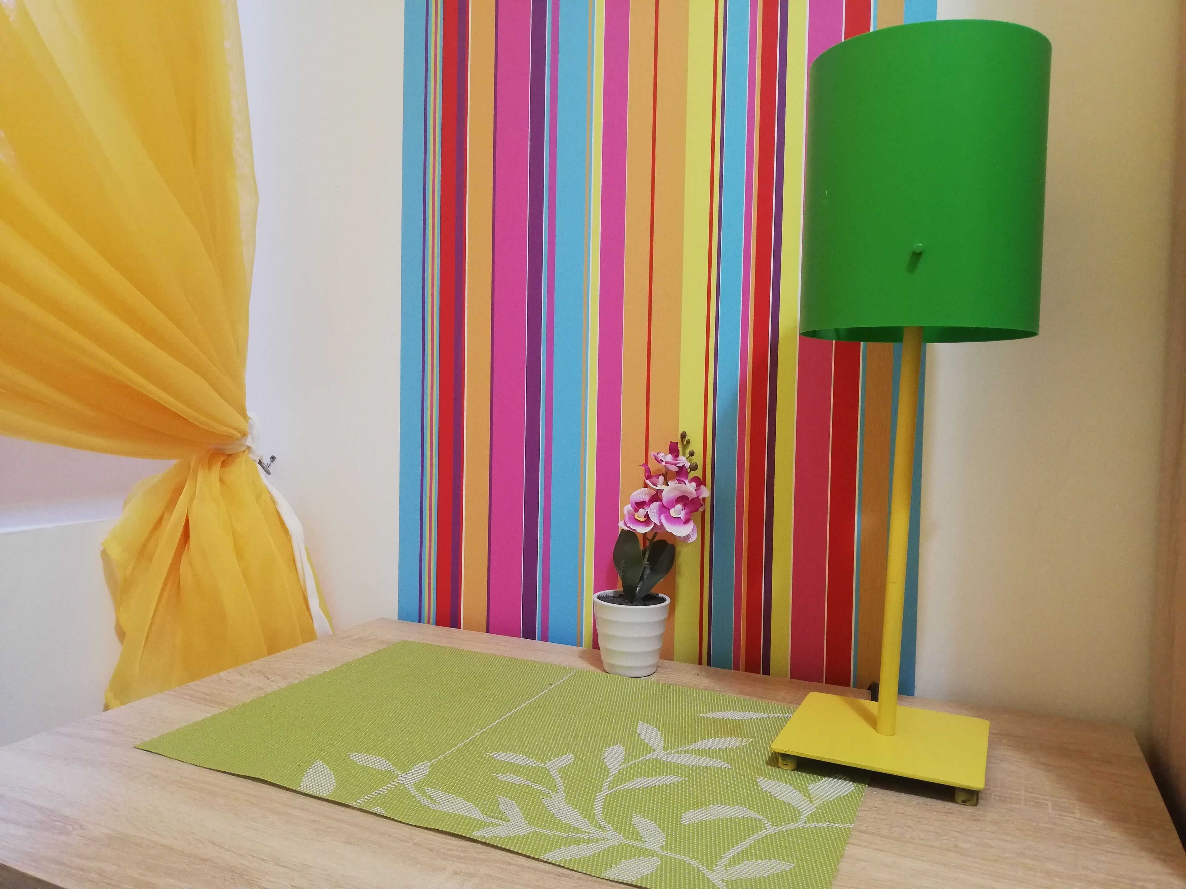 Una habitación con pared a rayas, un felpudo verde, una planta pequeña en maceta y una lámpara verde.