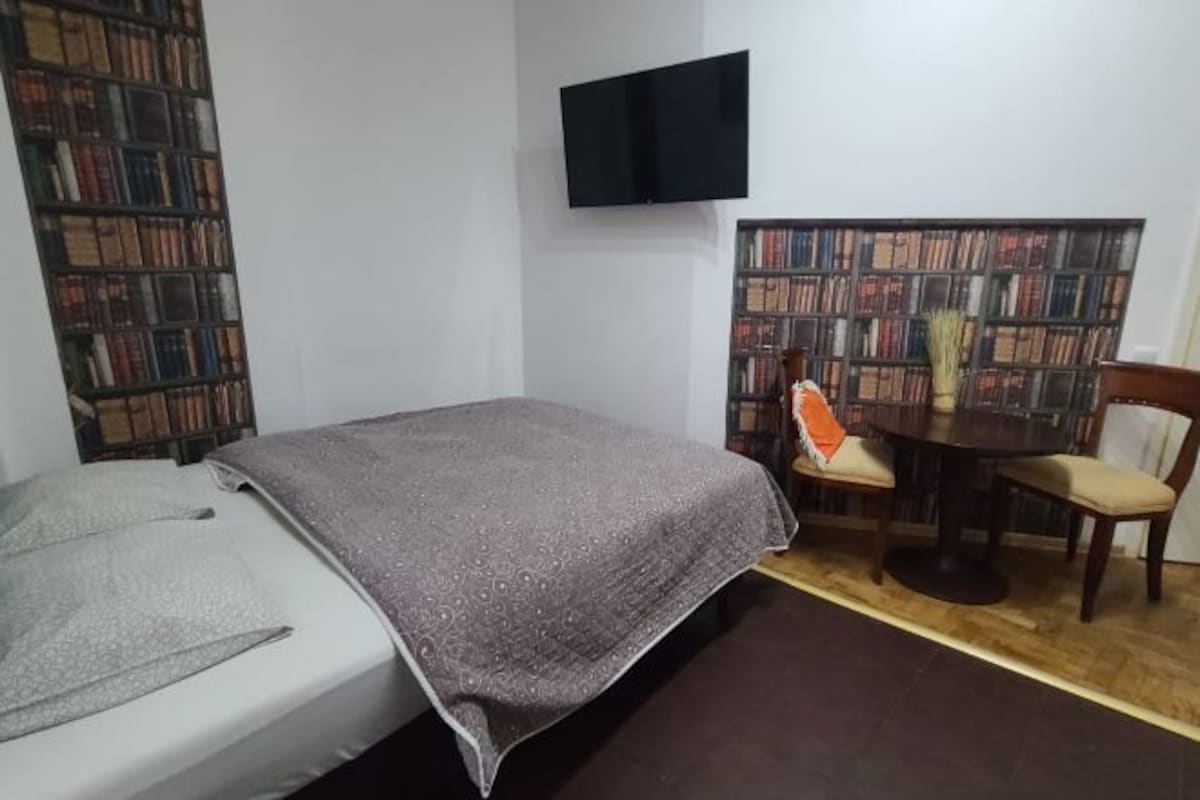 A bedroom with a bed, a desk with a chair, a bookshelf, and a flat-screen TV.