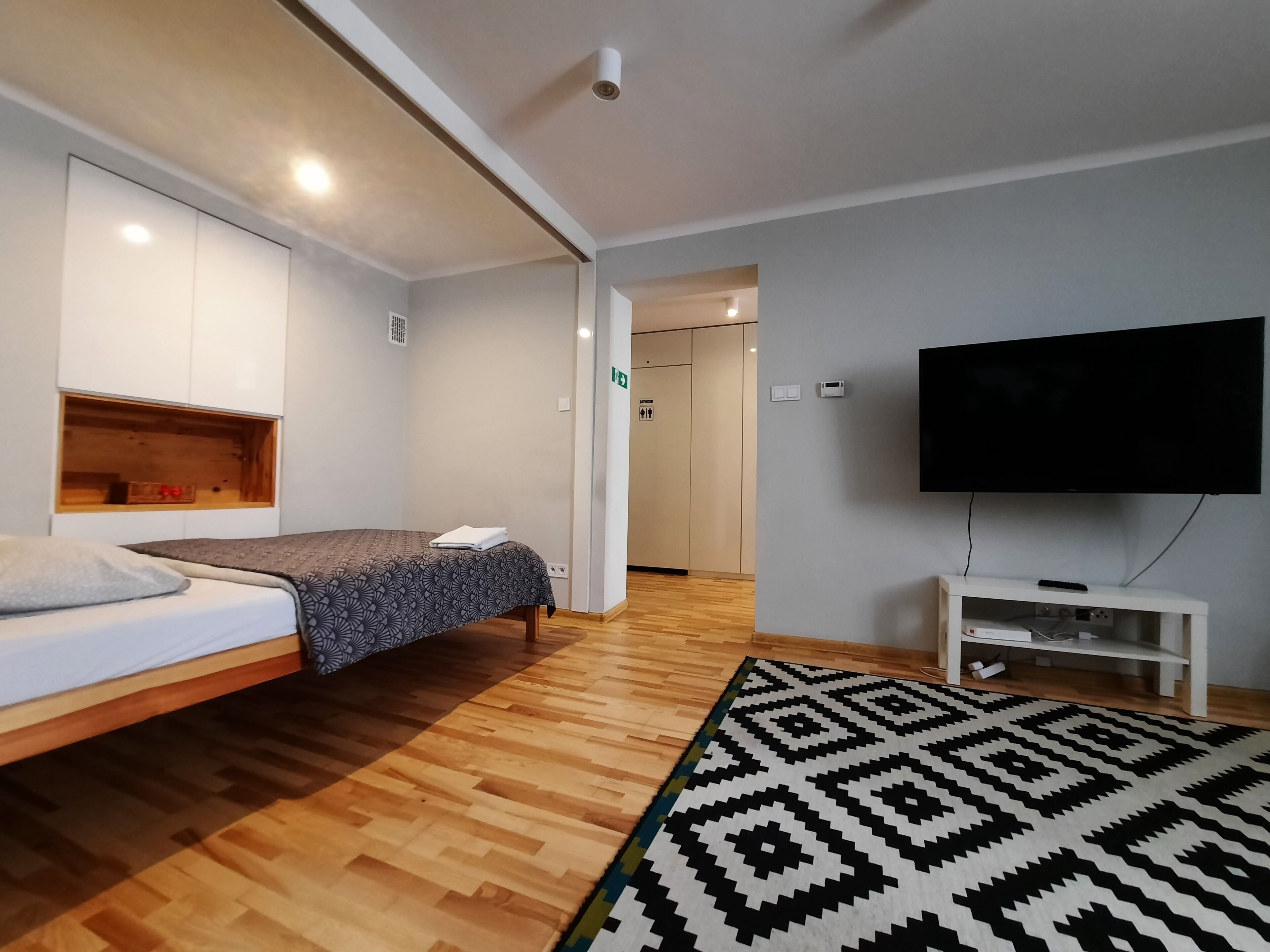 A modern room with a bed, a flat-screen TV, and a wooden floor.