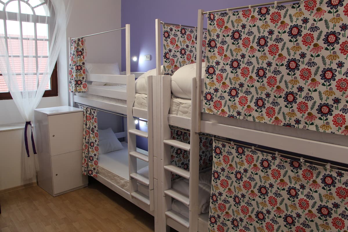 A room with bunk beds, a small desk, and a window with sheer curtains.
