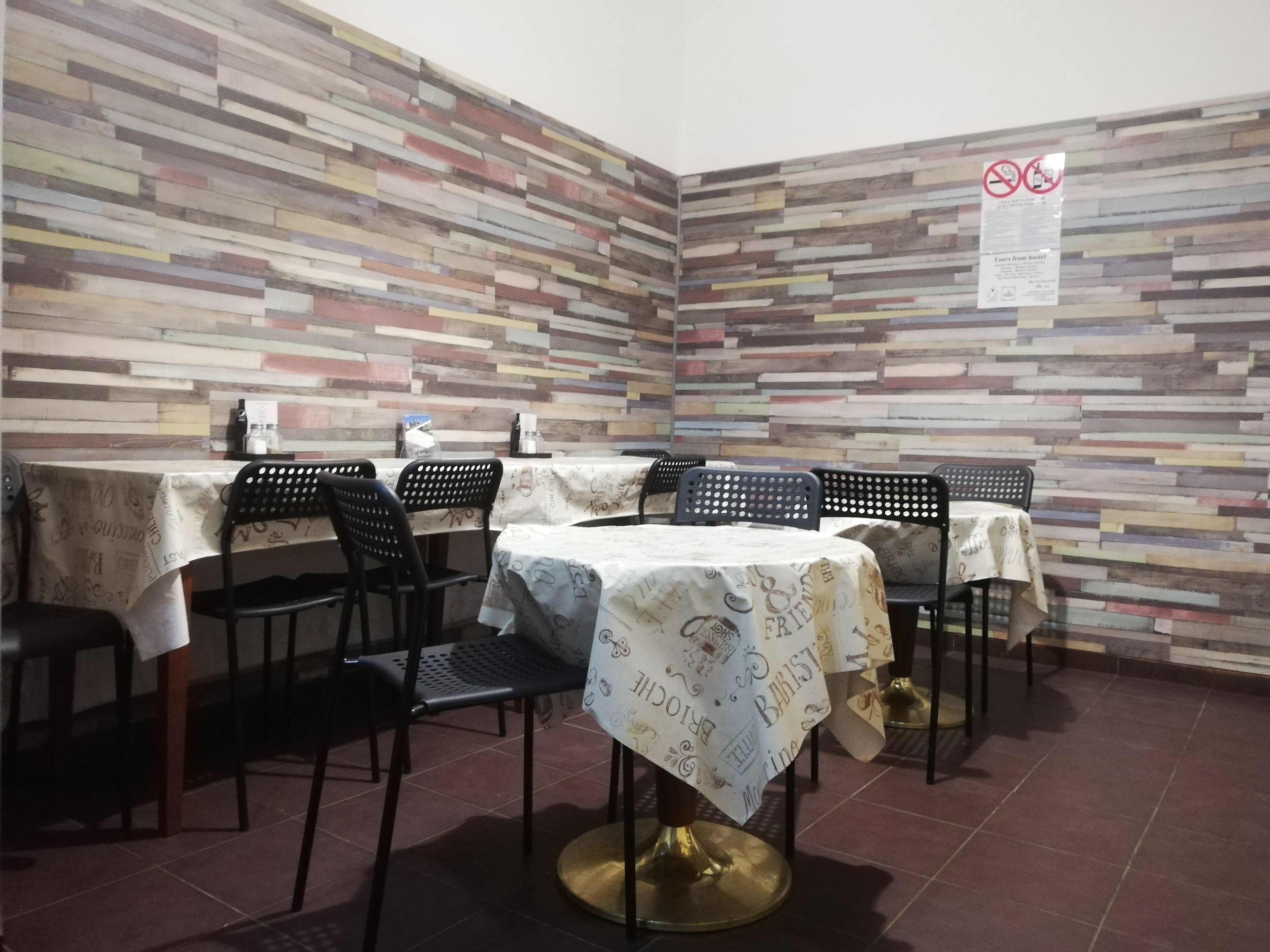 A restaurant with a modern, multicolored wooden wall design, tables with patterned tablecloths, and black chairs.
