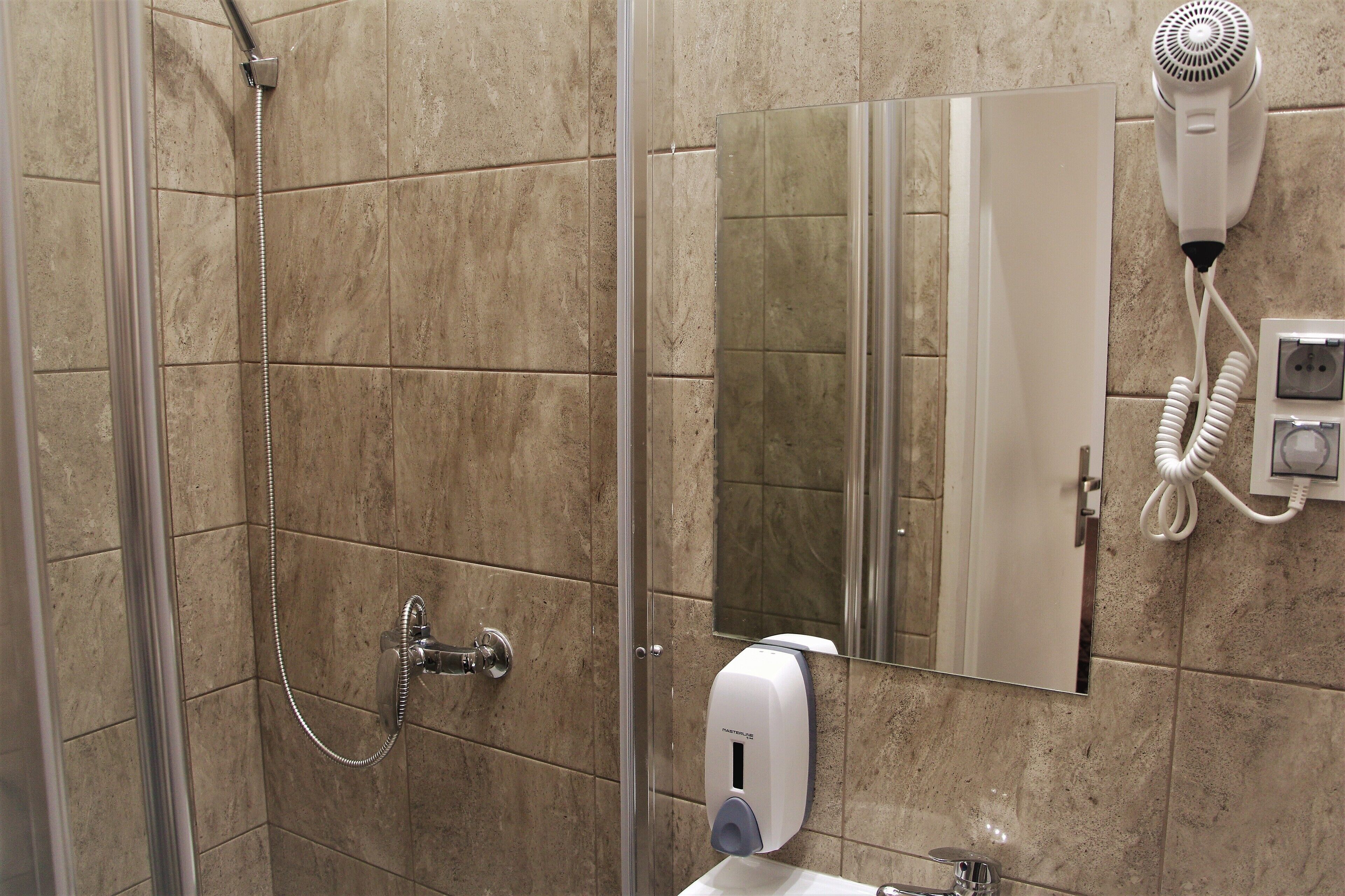 A bathroom with a shower, a hairdryer mounted on the wall, a hand dryer, and a mirror.