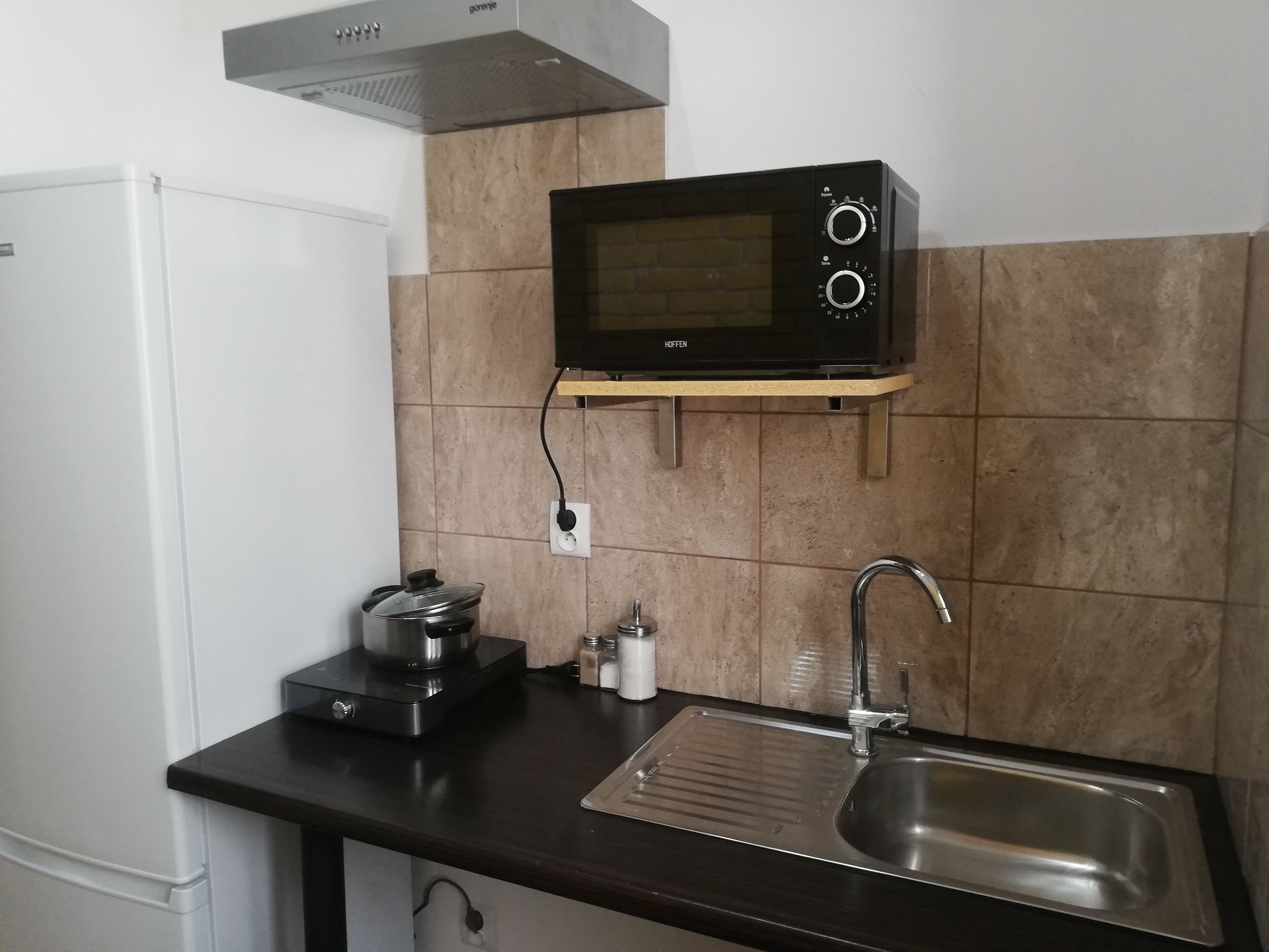 Una cocina compacta equipada con microondas, hervidor, pileta y cocina.