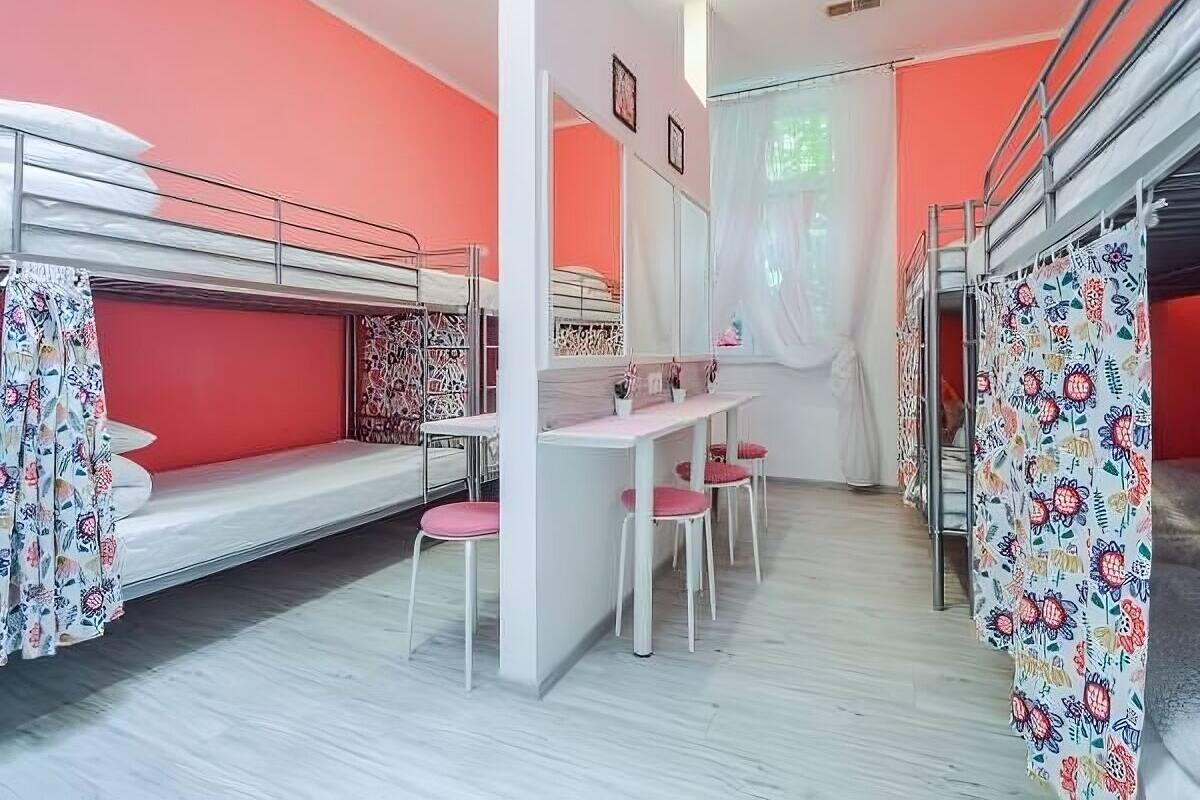 A dormitory room with bunk beds, a desk, chairs, and a mirror.