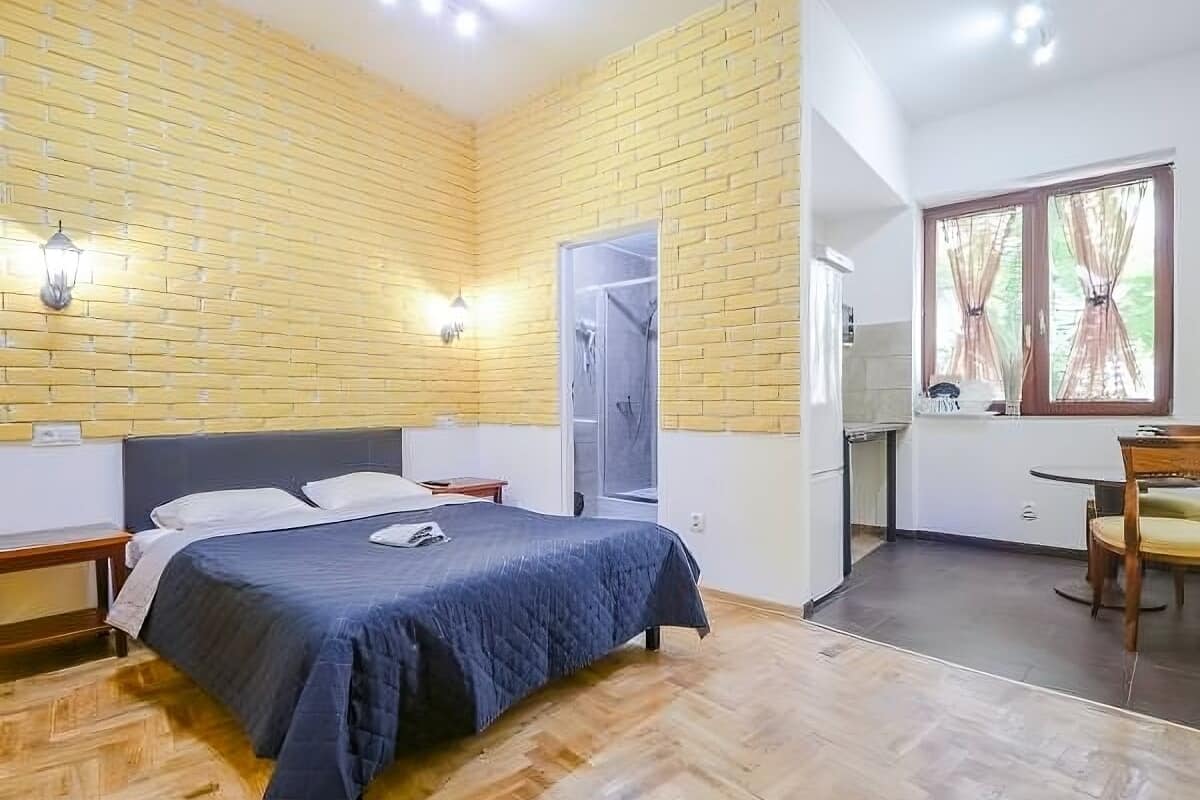 A bedroom with a bed, a nightstand, a wardrobe, a window with curtains, and a door leading to a bathroom.