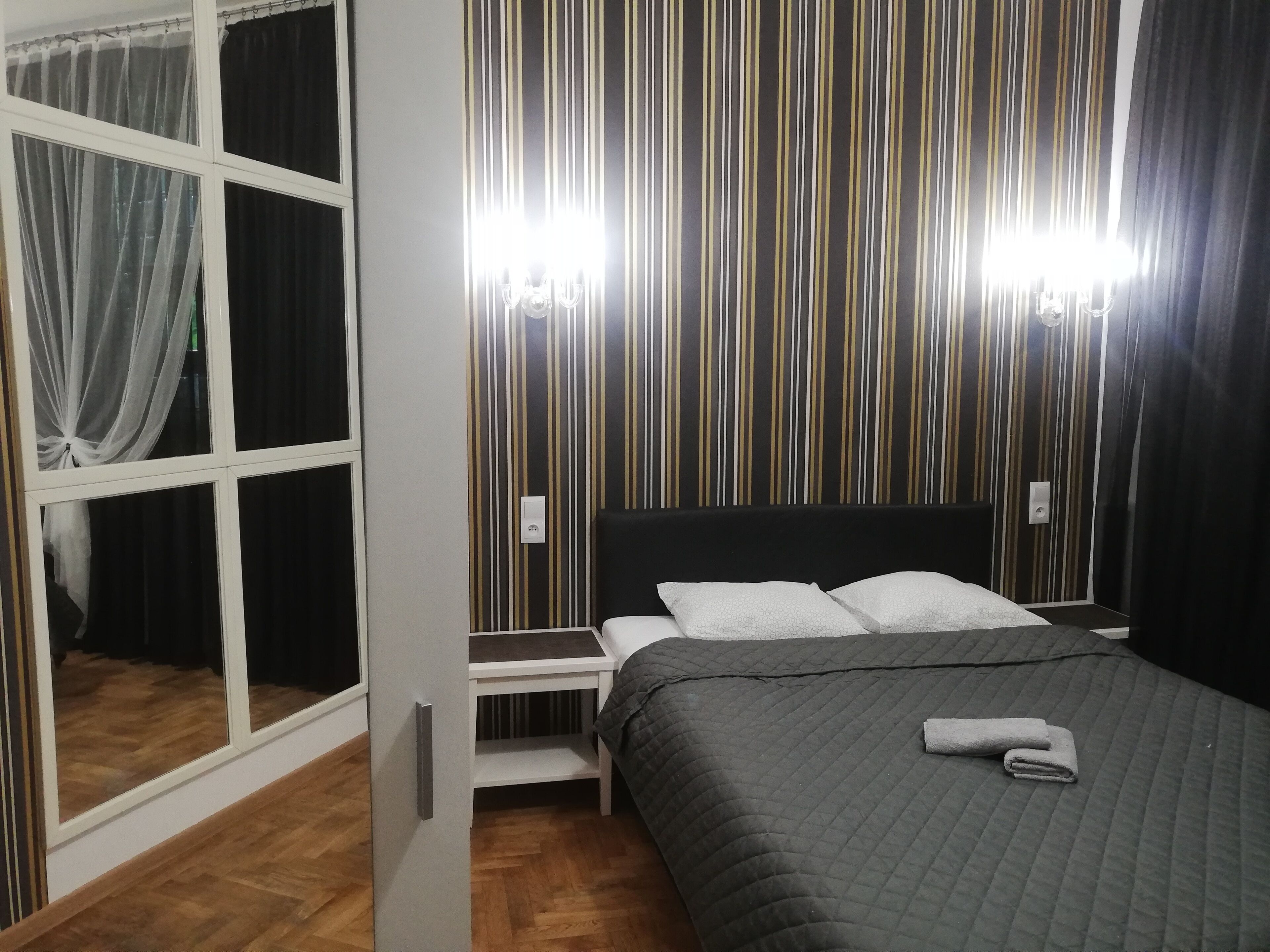 A bedroom with a bed, a nightstand, a window with curtains, and a striped wall.