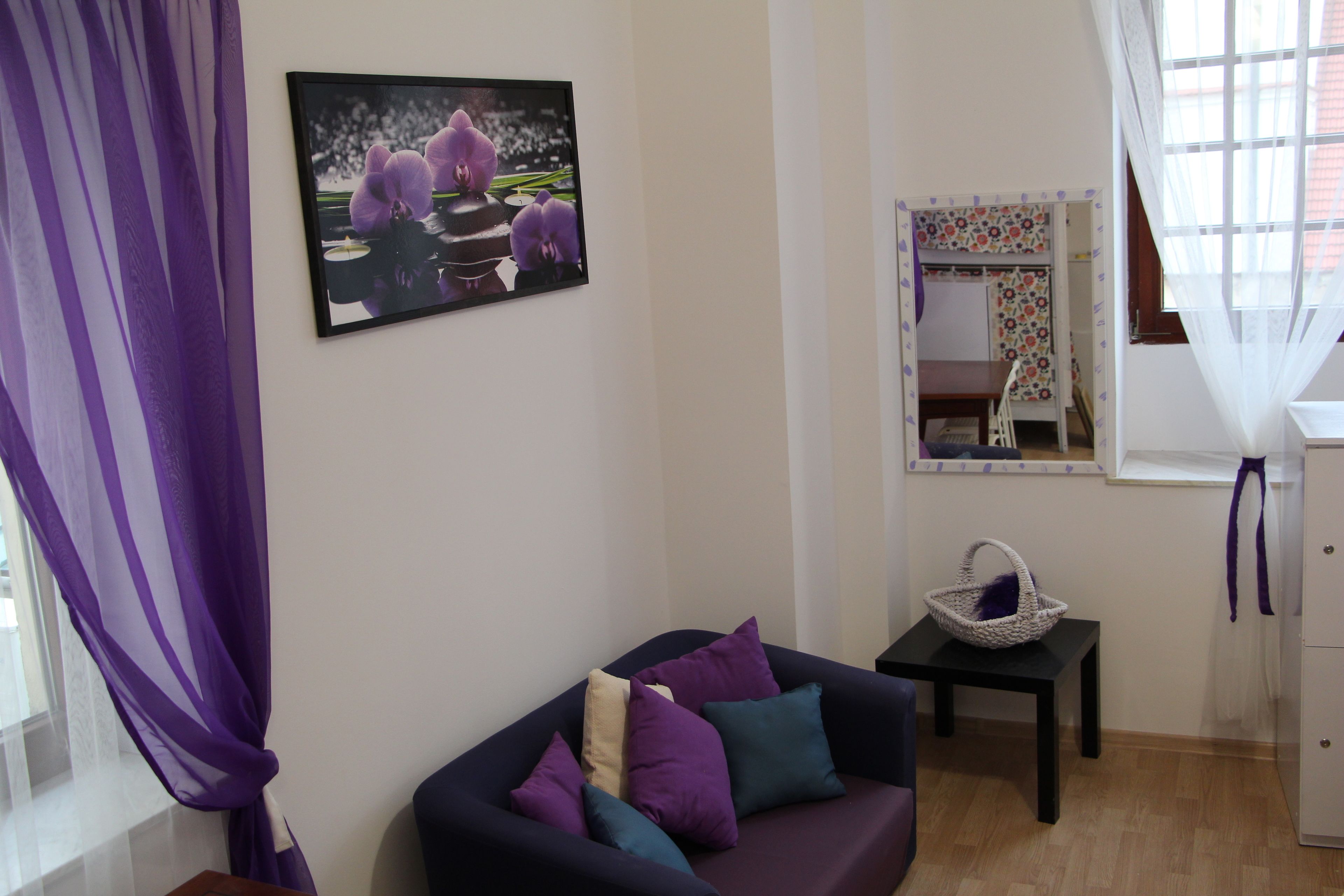 A living room with a sofa, a small table, a basket, and a window with curtains.