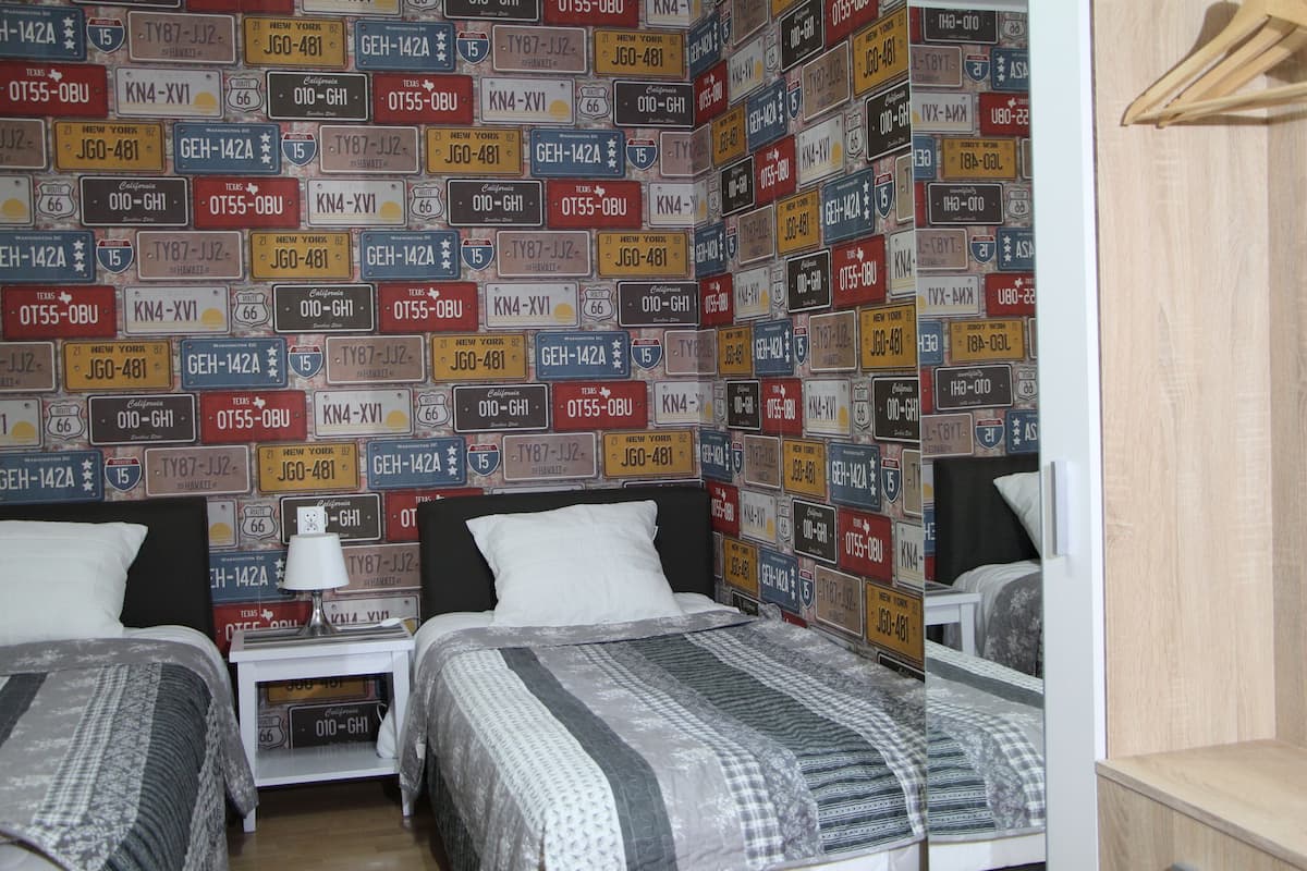 A room with two beds, a nightstand with a lamp, and a wall covered with license plates.