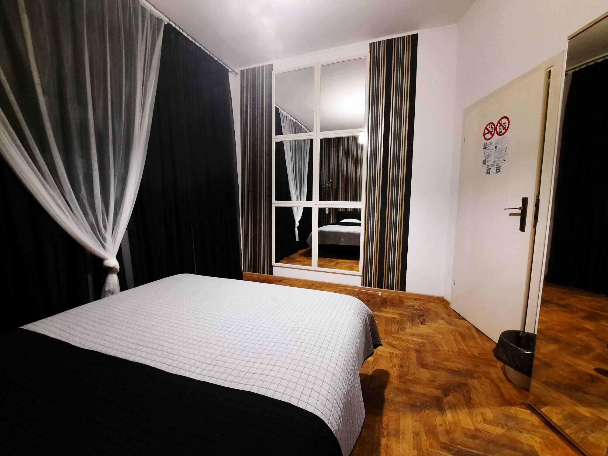 Une chambre à coucher avec un lit, une fenêtre avec des rideaux, une porte et un plancher en bois.