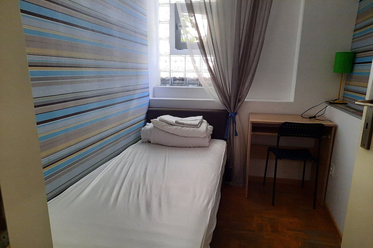 A small, neatly arranged room with a bed, a desk, and a chair.