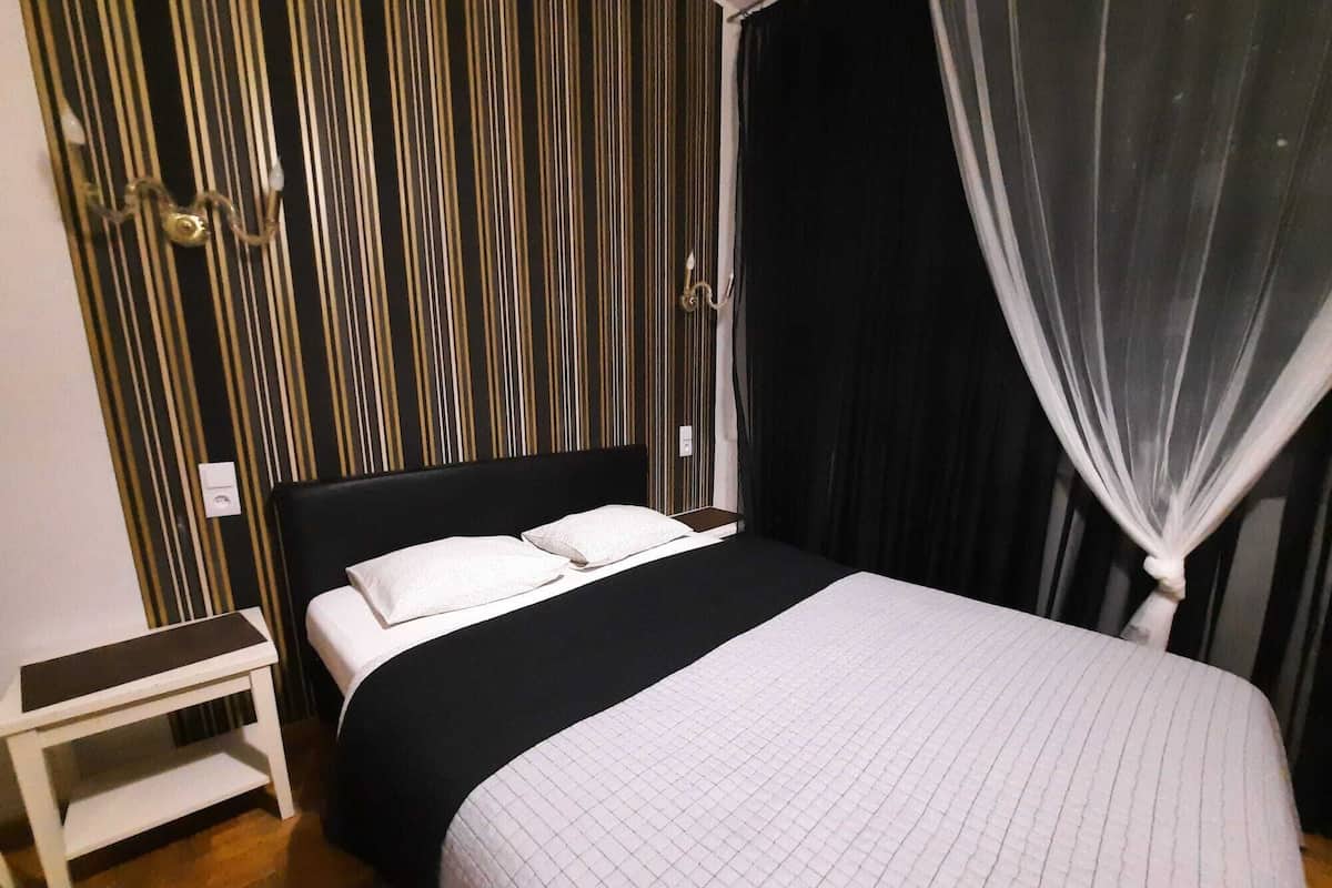 A neatly made bed with white linens, a black headboard, and a bedside table with a lamp.
