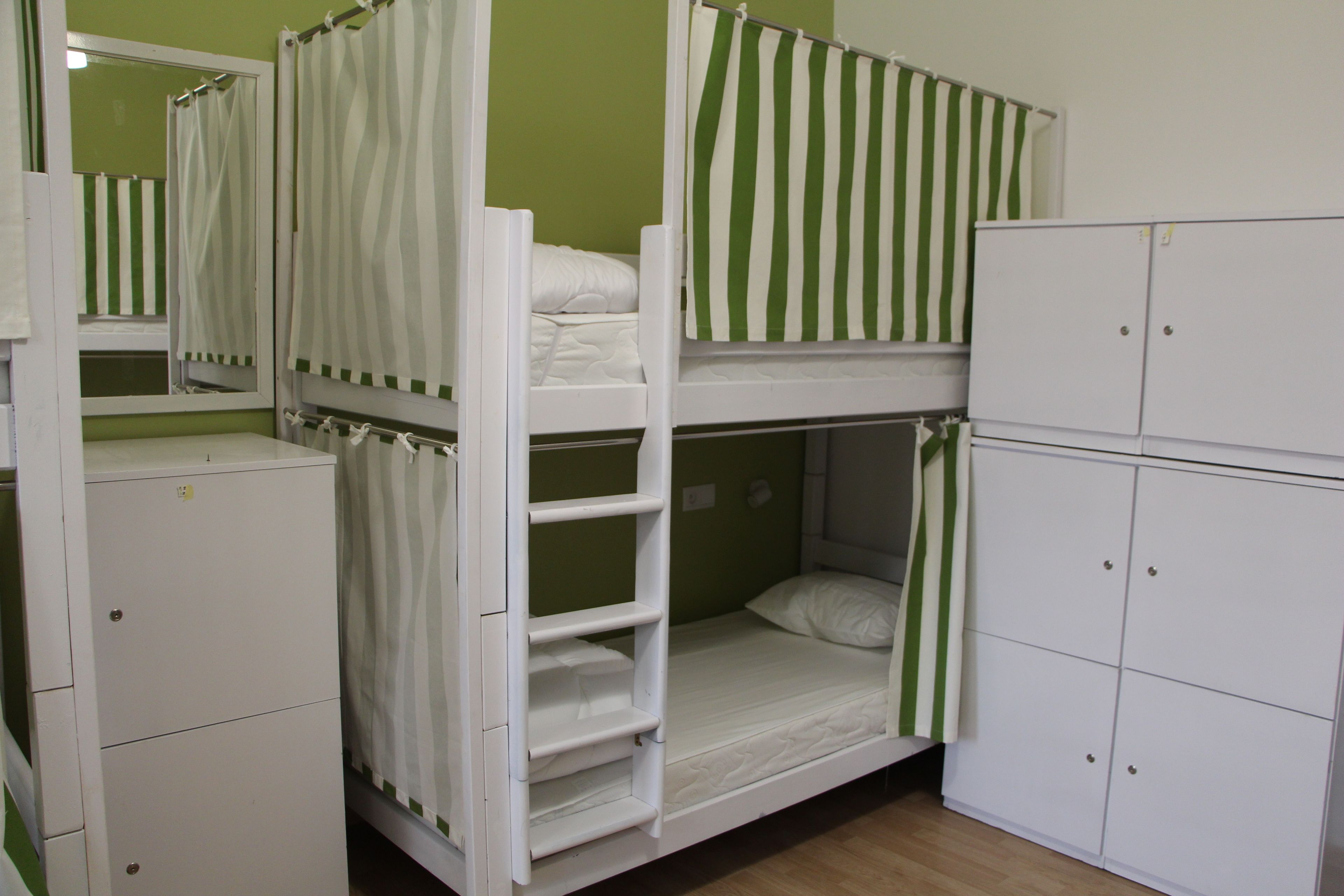 Una camera con letto a castello, parete verde, mobili bianchi e tende a righe.