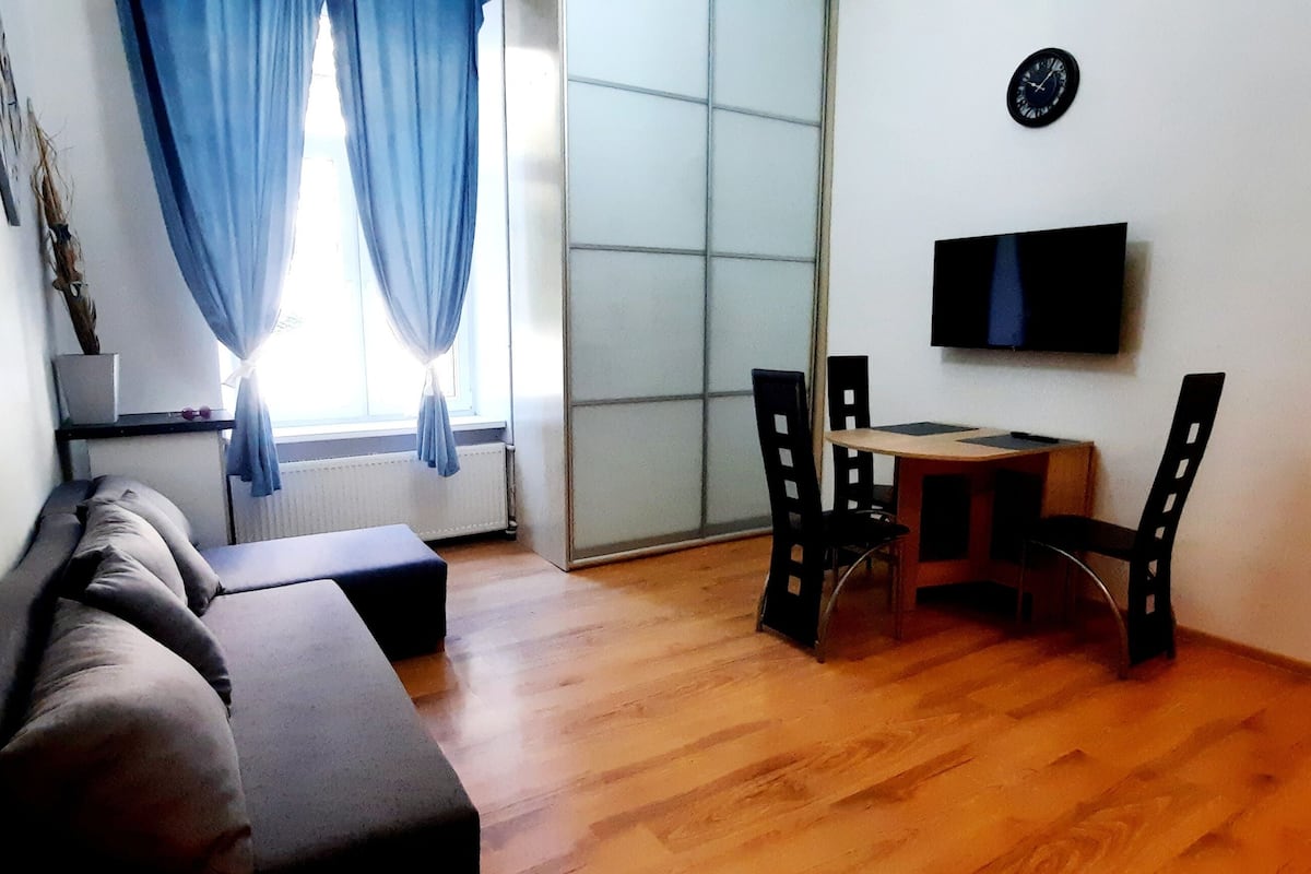 A living room with a sofa, a small table, and a TV mounted on the wall.