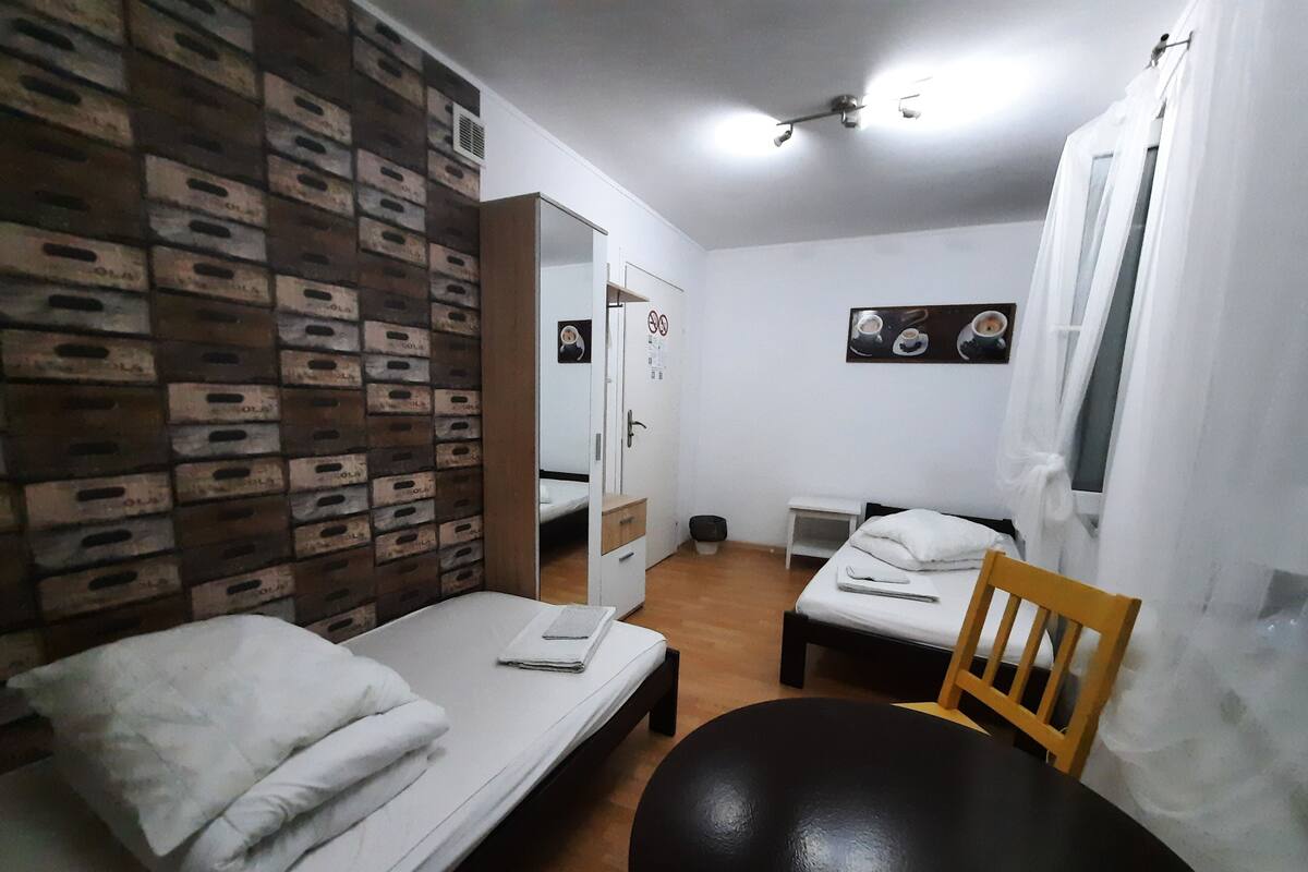 A room with two beds, a wooden chair, a small table, and a wall with a patterned design.
