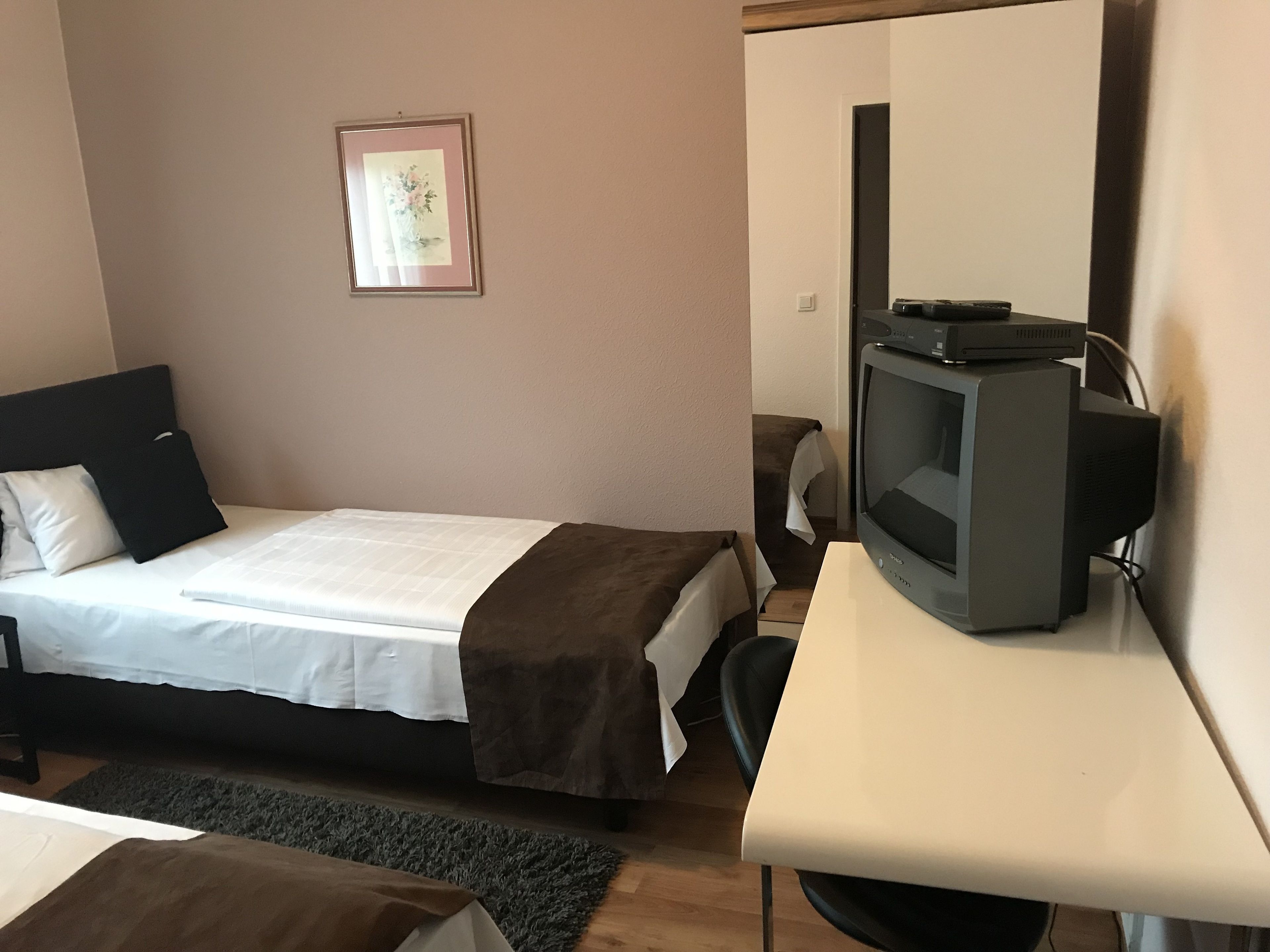 A bedroom with a bed, a television on a stand, a chair, and a framed picture on the wall.