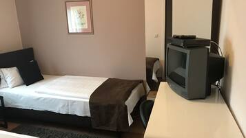 A bedroom with a bed, a television on a stand, a chair, and a framed picture on the wall.