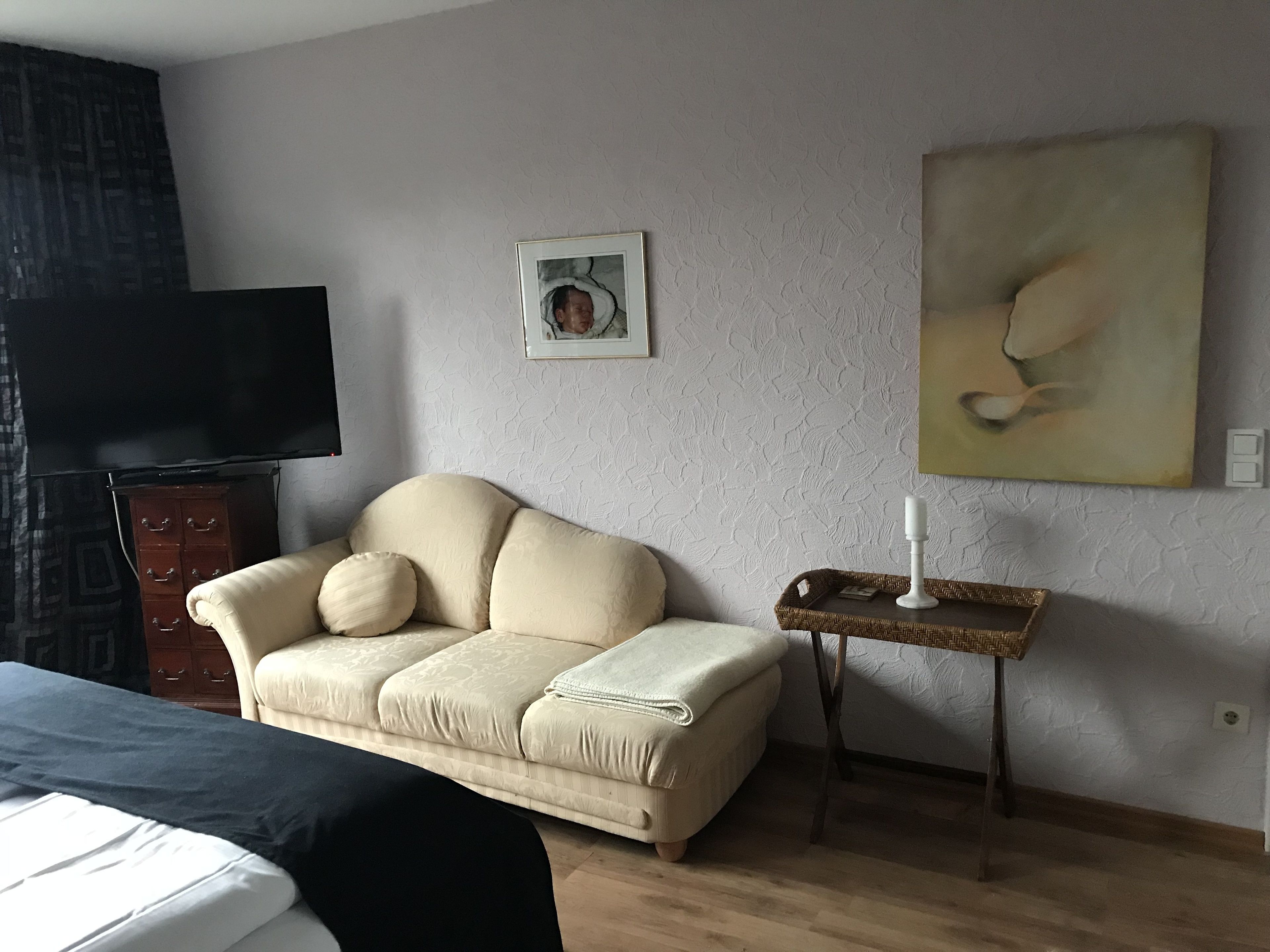 A room with a sofa, a TV, a small table with a candle, and a painting on the wall.