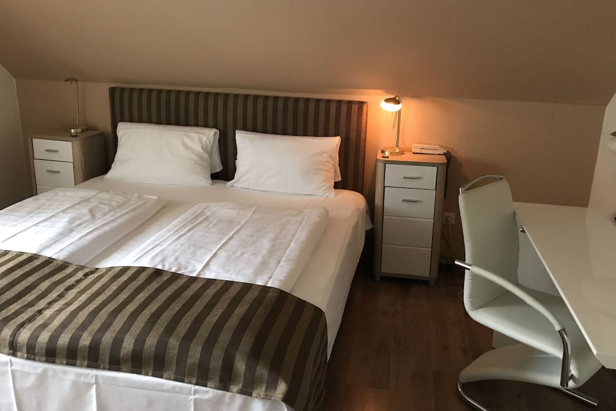 A neatly arranged hotel room with a bed, bedside tables, a desk, and a chair.