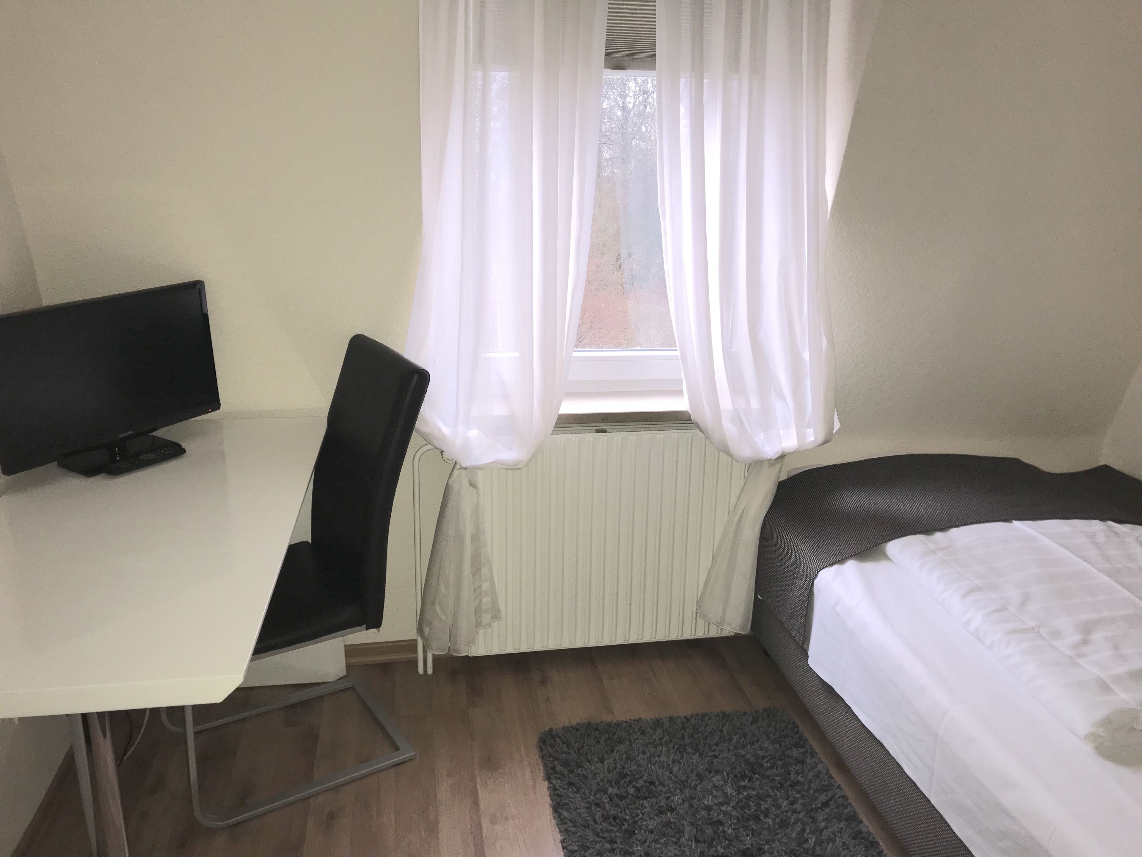 Una habitación pequeña y ordenada, con escritorio, silla y cama.