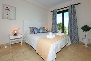 A neatly arranged bedroom with a bed, bedside table, lamp, and a view of greenery outside. - Villa Salobre Morro Golf 2 (Maspalomas)