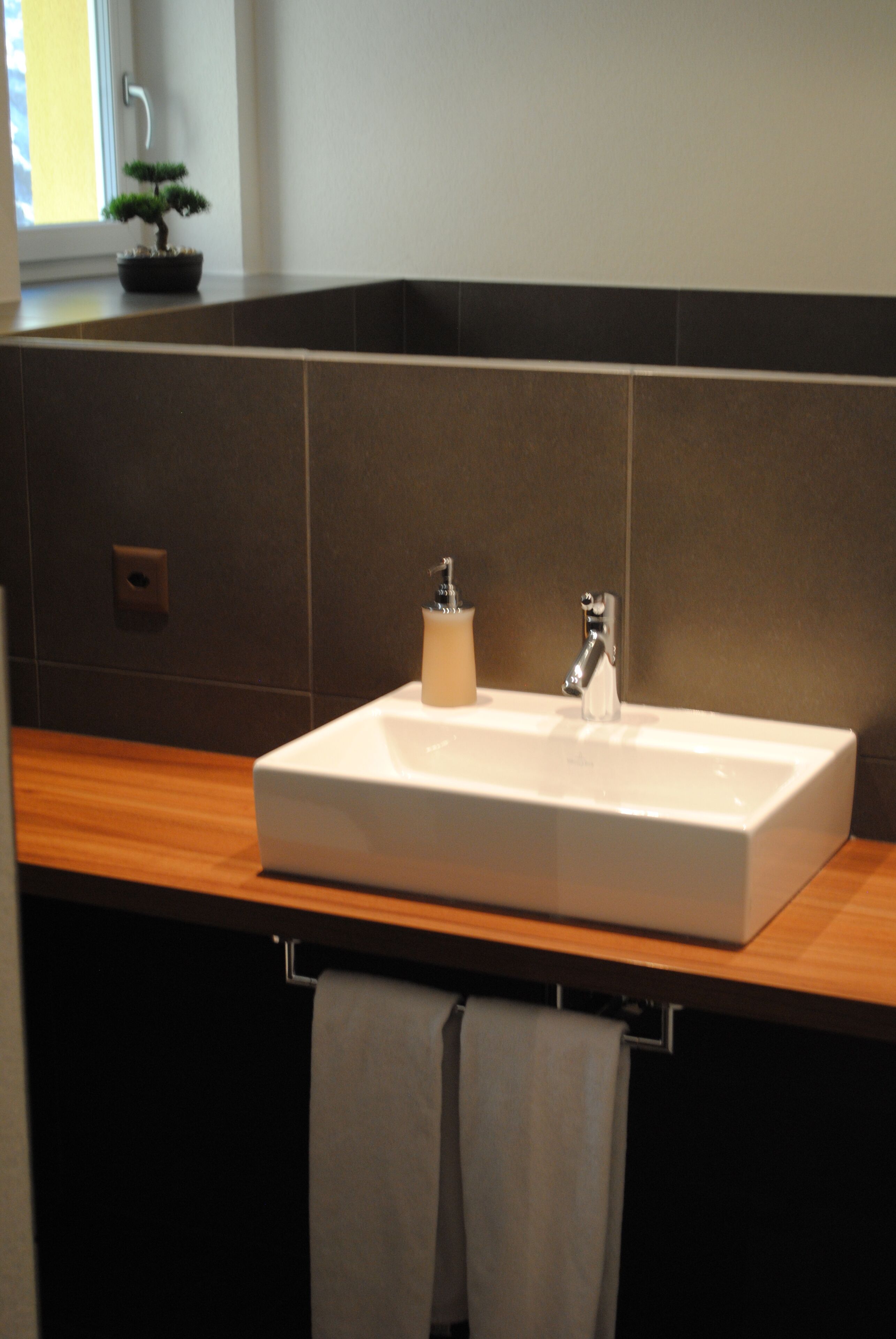 A bathroom with a white sink, a small potted plant, and a towel hanging on a rack.