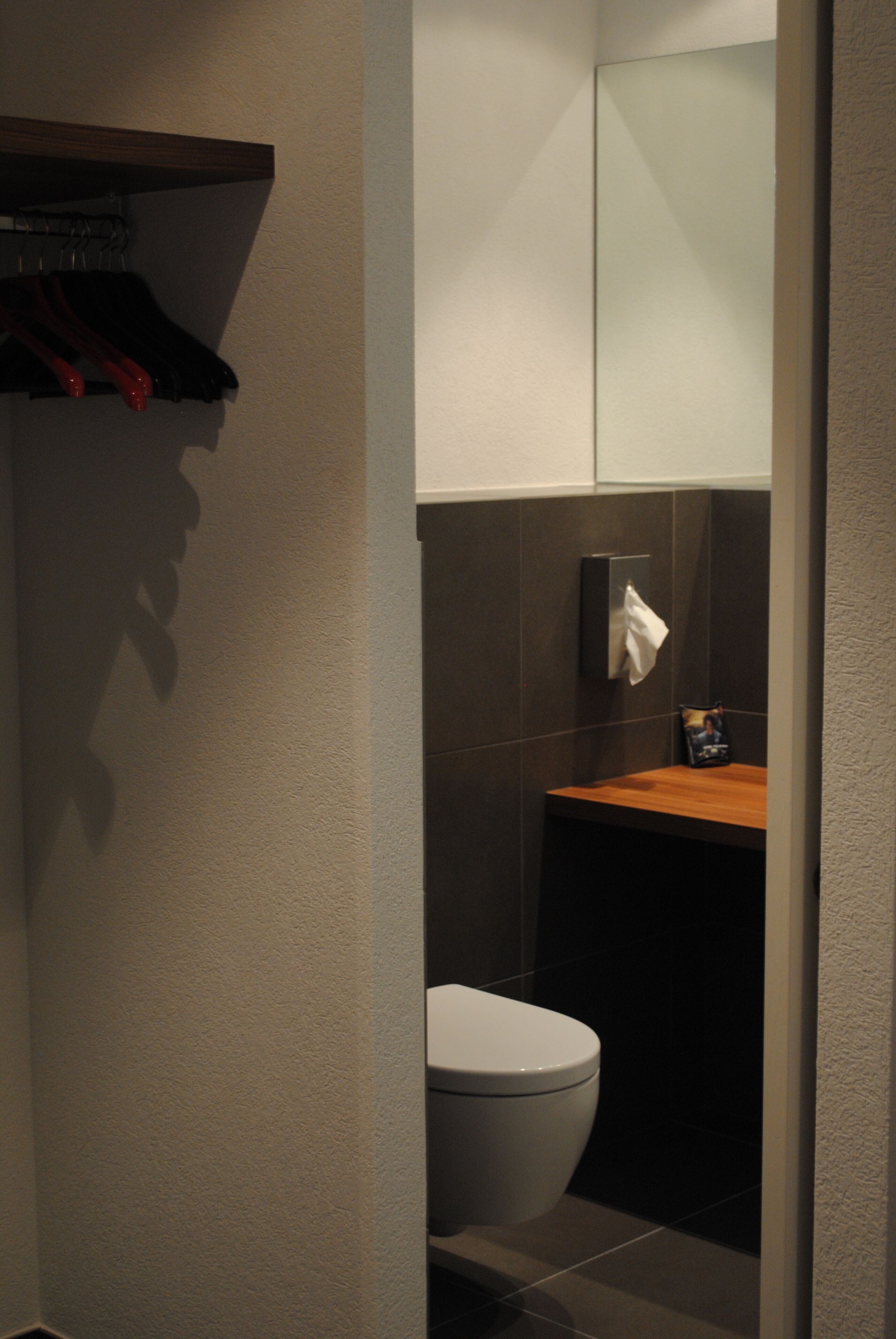 Une salle de bain moderne équipée de toilettes, d’un distributeur de serviettes et d’une étagère sur laquelle sont suspendus divers objets.