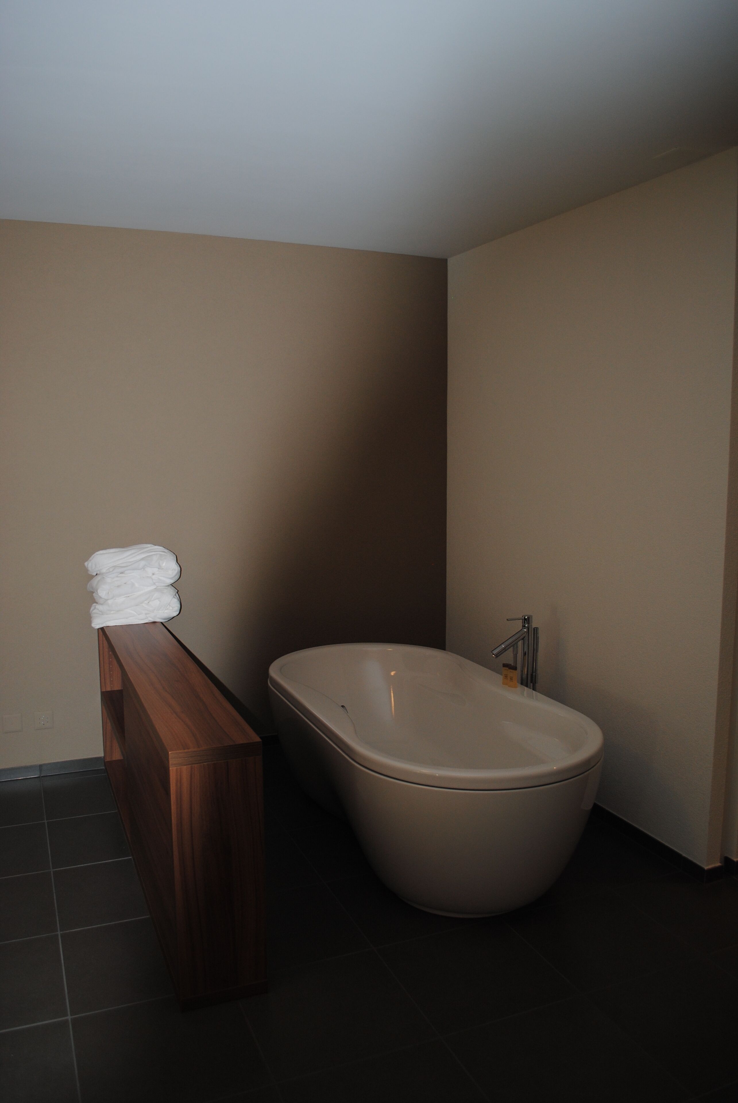 Et badeværelse med en træbænk, et hvidt badekar og et toilet.