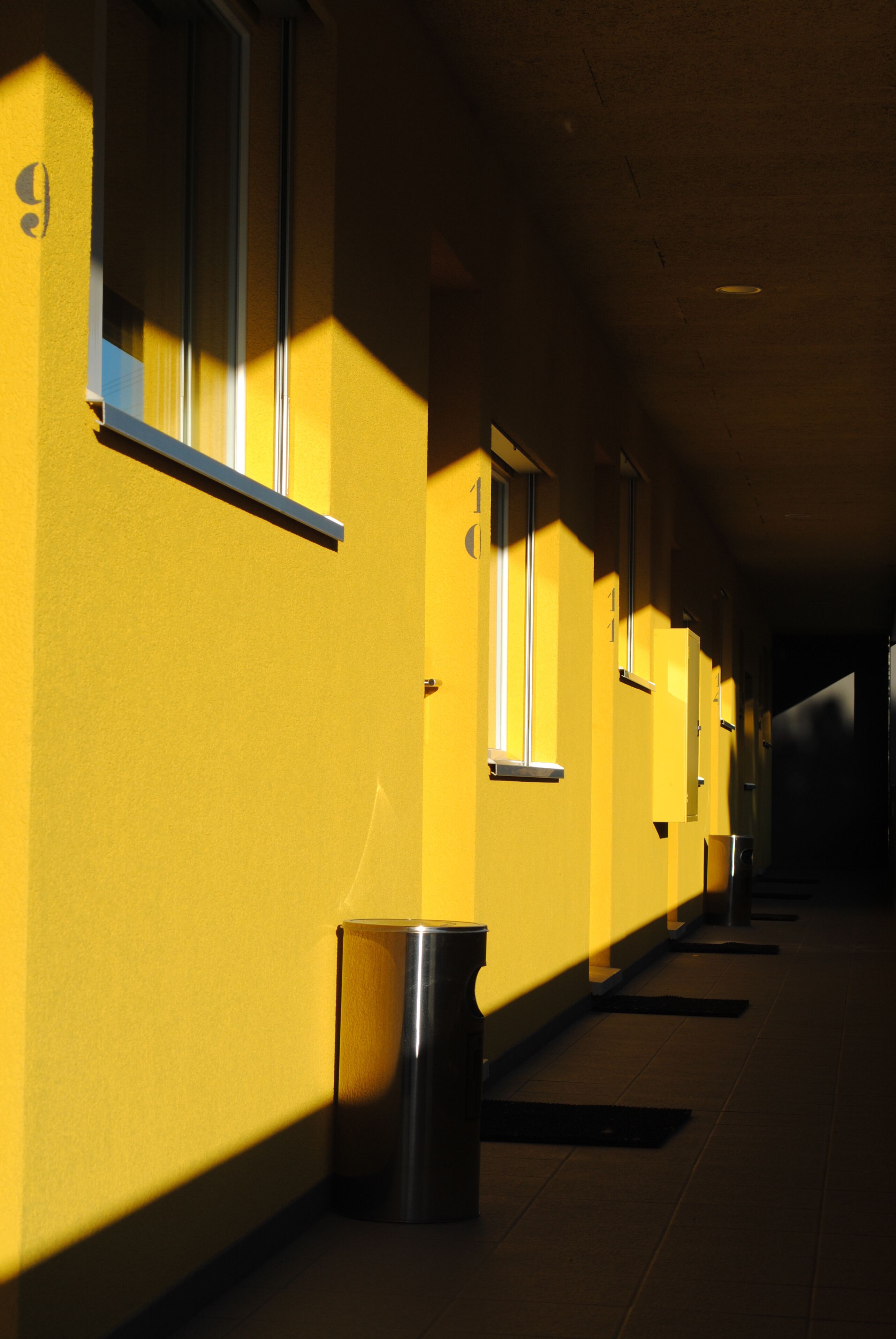 A corridor with yellow walls and windows, a trash bin, and a ceiling light fixture.