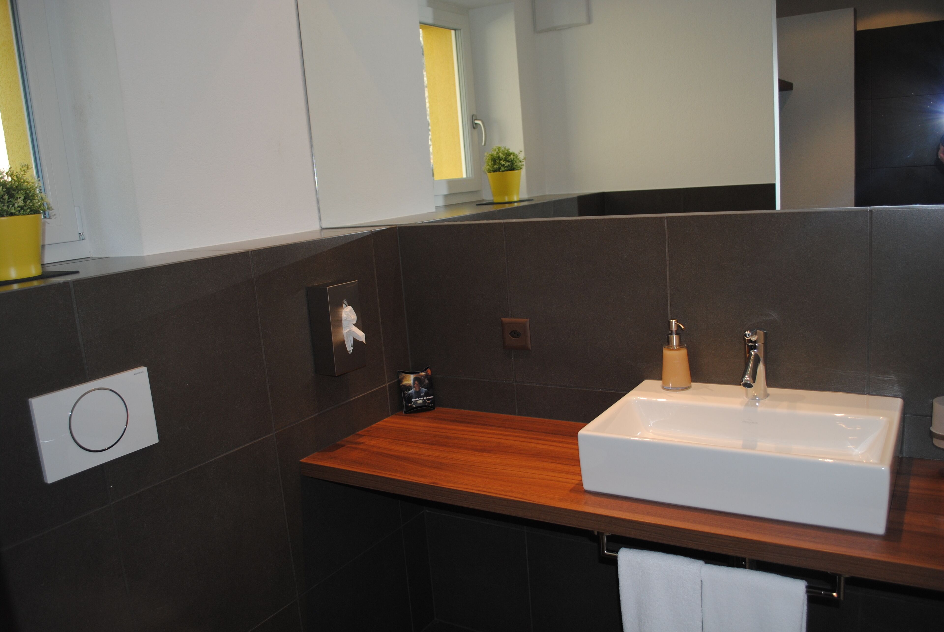 A modern bathroom with a wooden vanity, a white sink, and a mirror.