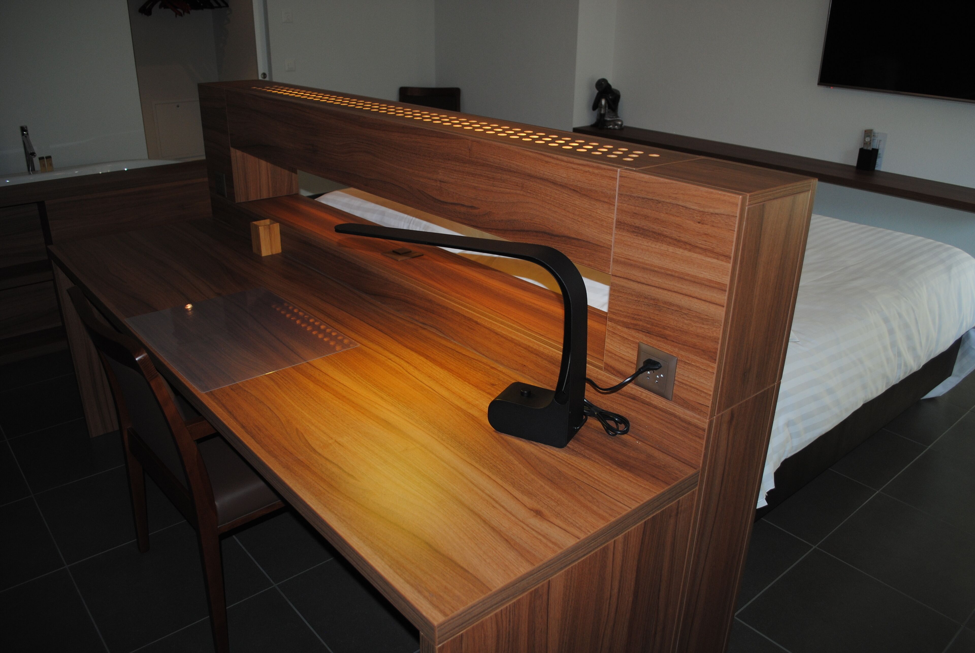 Una habitación de hotel moderna con un escritorio de madera, una silla, una cama con ropa de cama blanca y un televisor de pantalla plana montado en la pared.