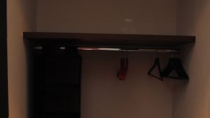 A small closet with shelves and hanging space, a bench, and a door.
