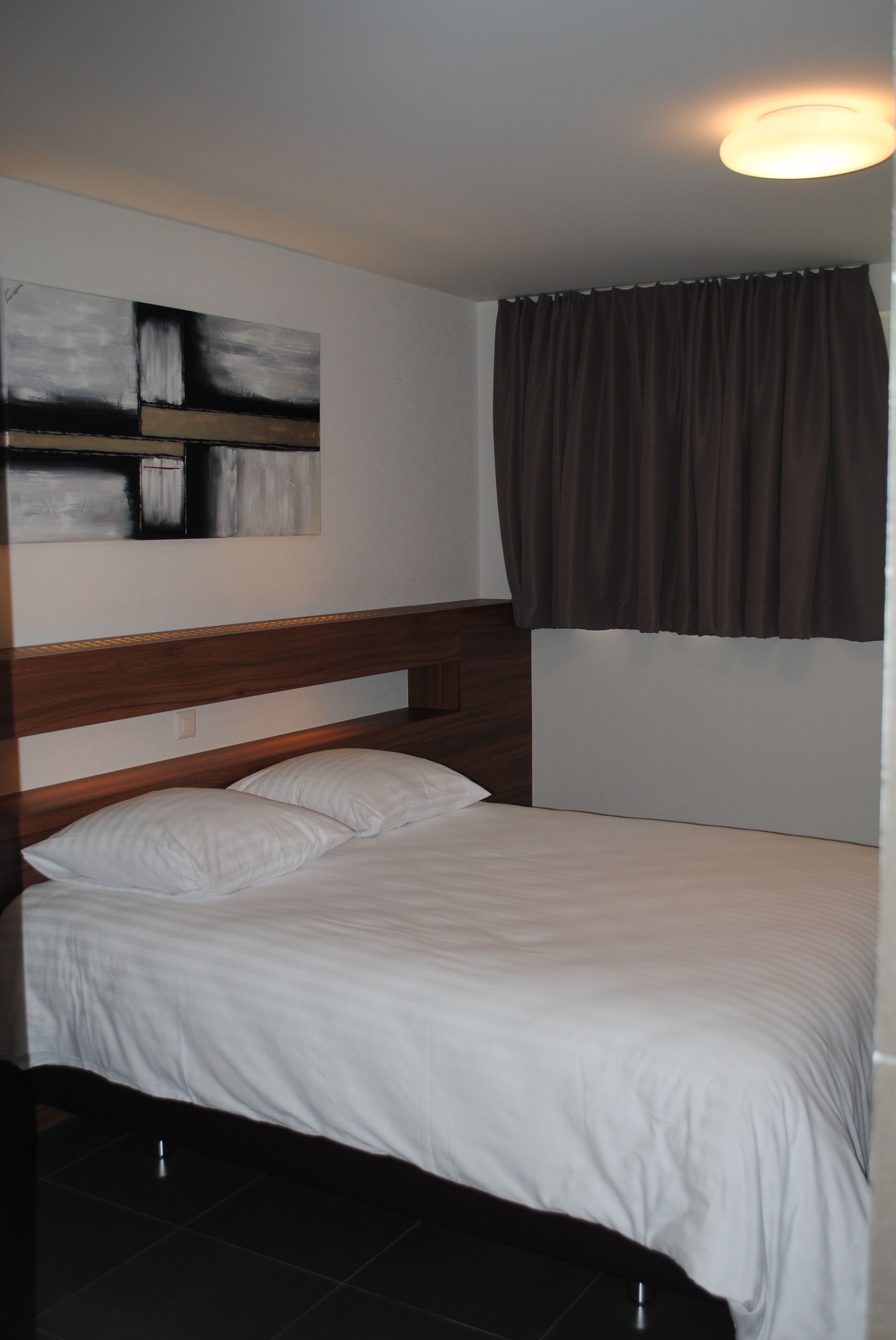 A neatly made bed with white linens, a wooden headboard, and a modern abstract painting on the wall.