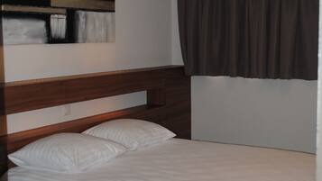 A neatly made bed with white linens, a wooden headboard, and a modern abstract painting on the wall.
