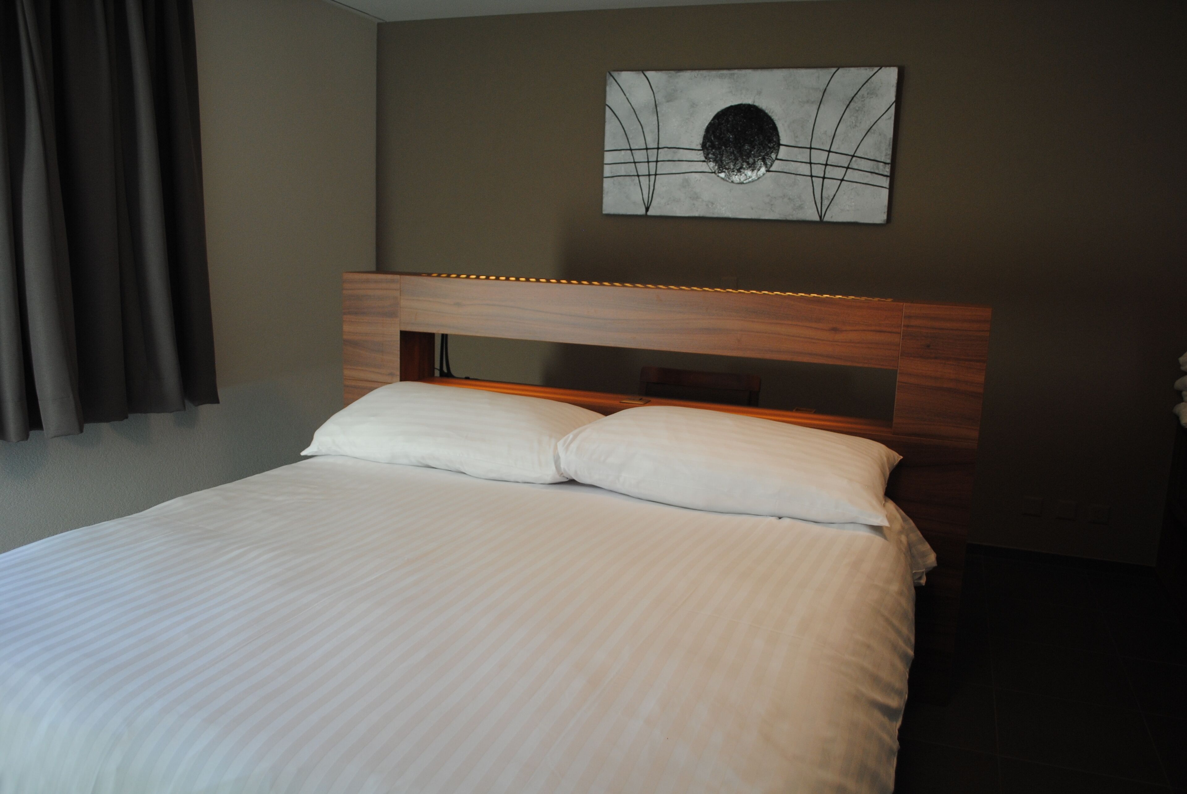 Una cama bien hecha con cabecera de madera y un cuadro colgado encima.