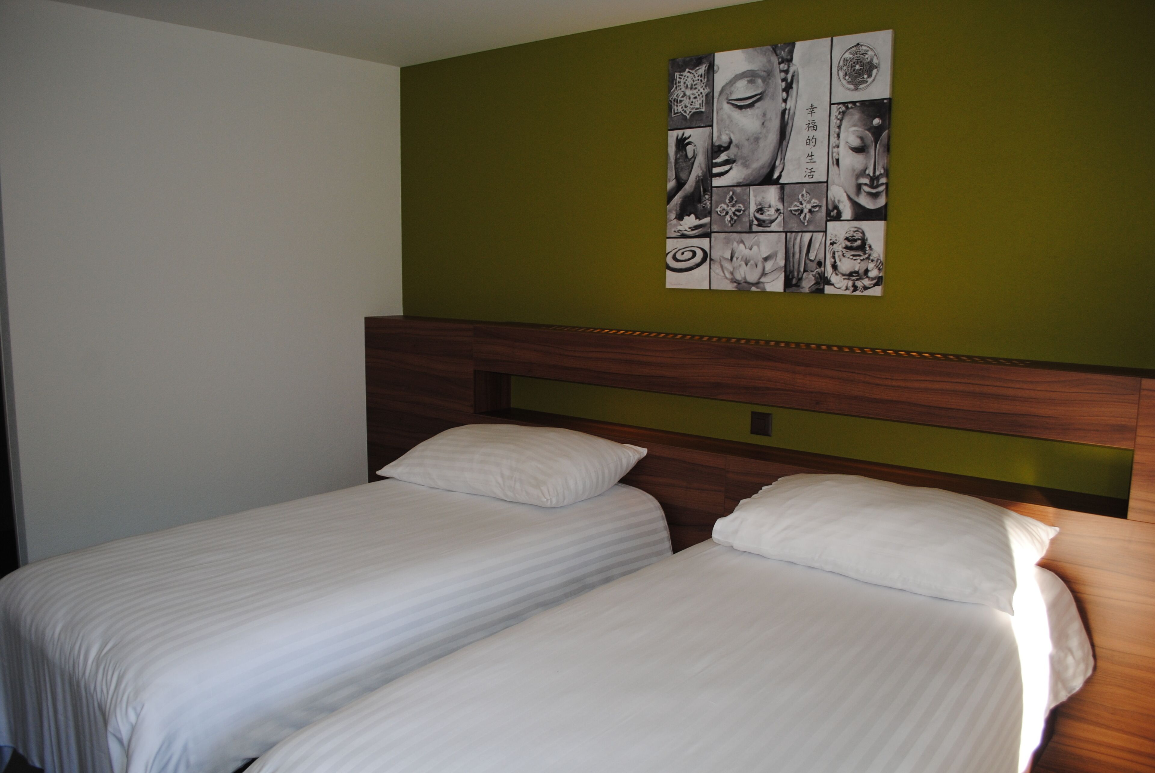 A hotel room with two single beds, a wooden headboard, and a wall art piece above the beds.
