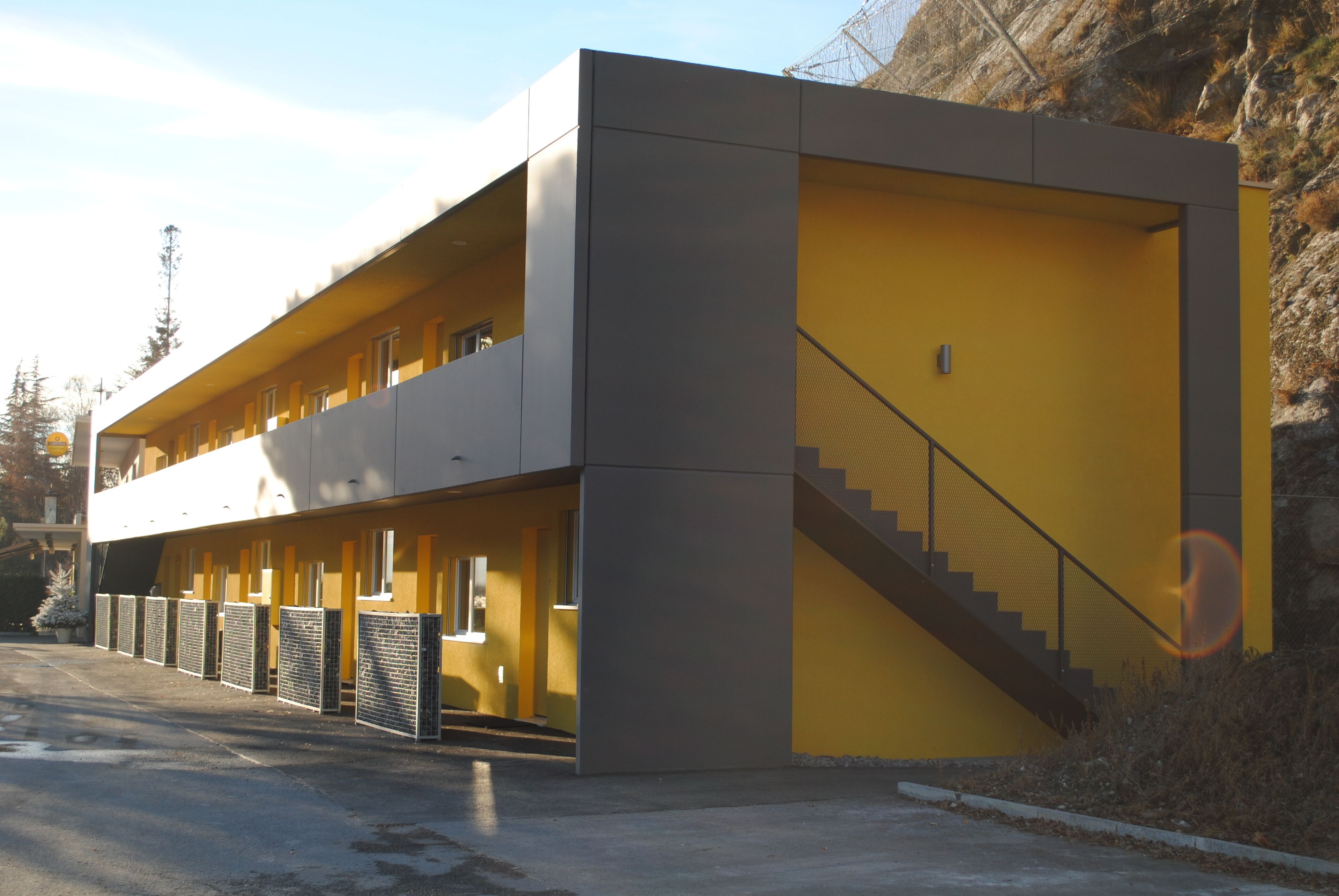 A modern building with a yellow facade, a staircase, and a covered outdoor area.