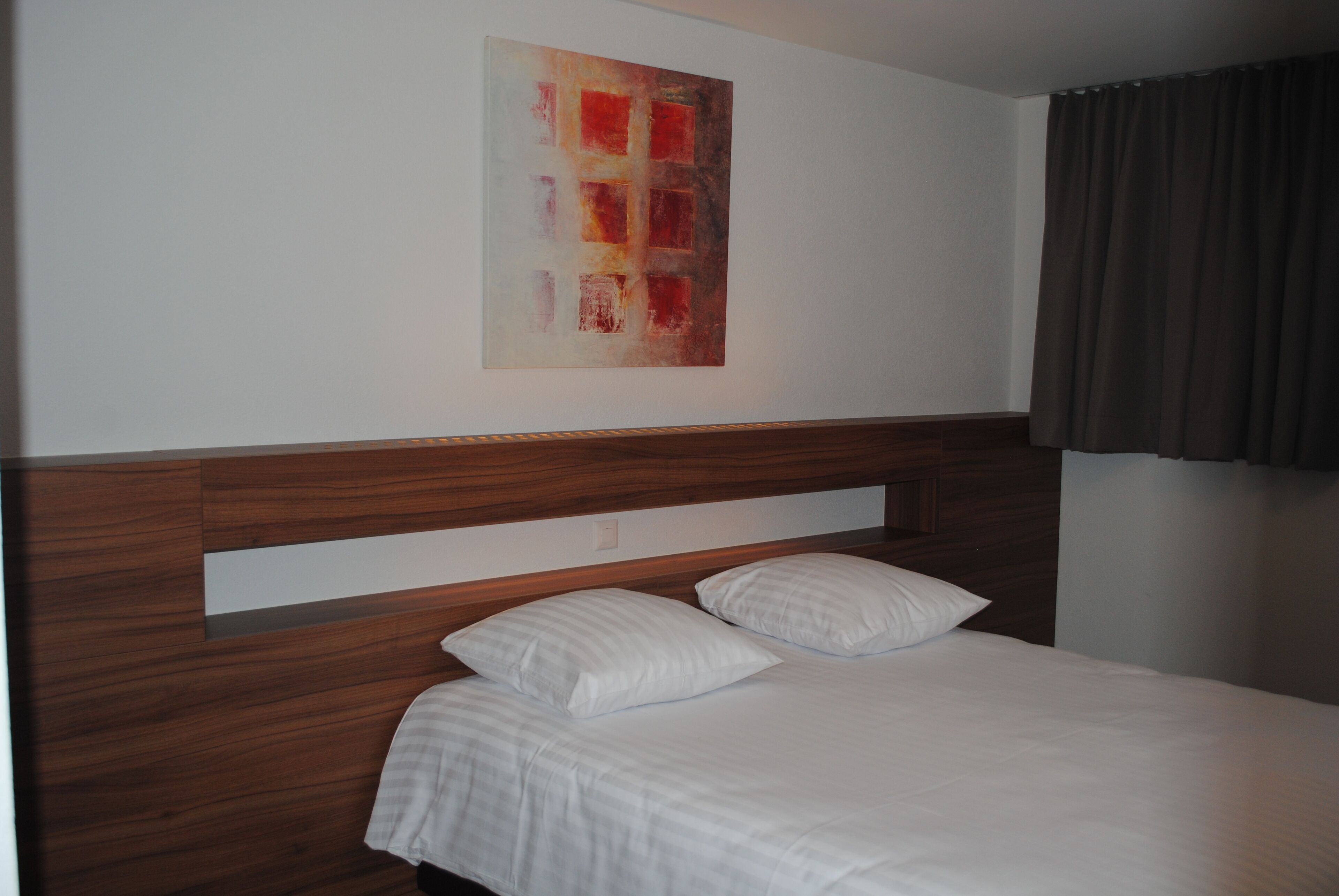 Una habitación de hotel con cabecera de madera, cama con ropa blanca y un cuadro abstracto grande en la pared.